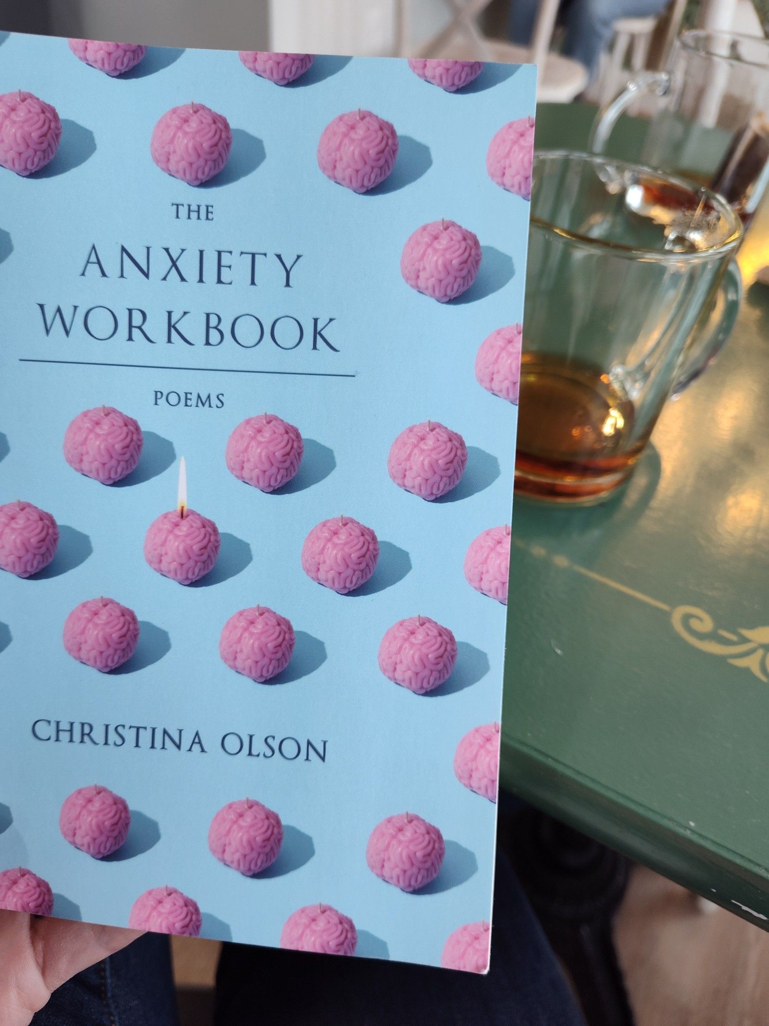 Photo of The Anxiety Workbook by Christina Olson in front of a green table with a mug of tea in the background.