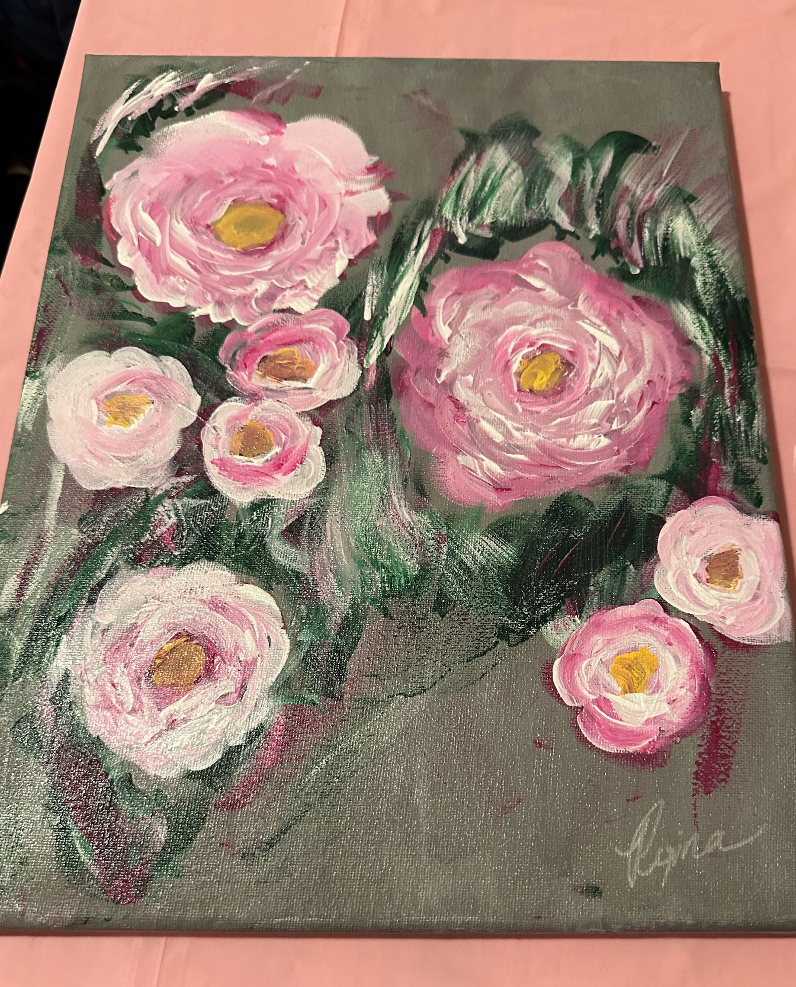 Final painting of pink peonies on a muted grey background. The medium is acrylic on canvas. It’s on a small table with a pink cover.