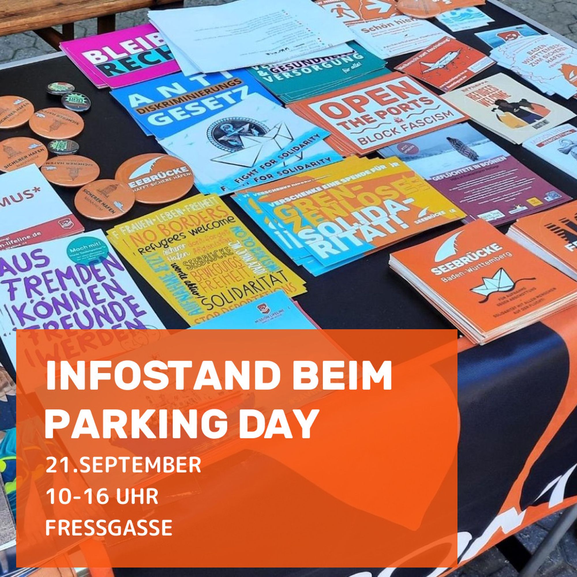 In the picture: Information stand with various stickers and buttons, postcards, information material from e.g. Amnesty and Seebrücke. At the bottom, an orange text field comes into the picture from the left. It reads: ‘Information stand at Parking Day’ and ‘21 September 10 am - 4 pm, Fressgasse