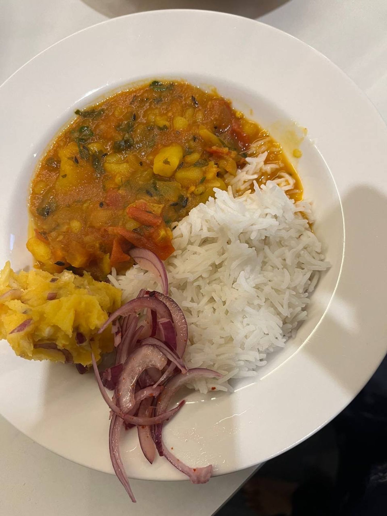 A bowl of rice, aaloo-tamatar jhol gravy, pickled onions, and aaloo bharta for lunch