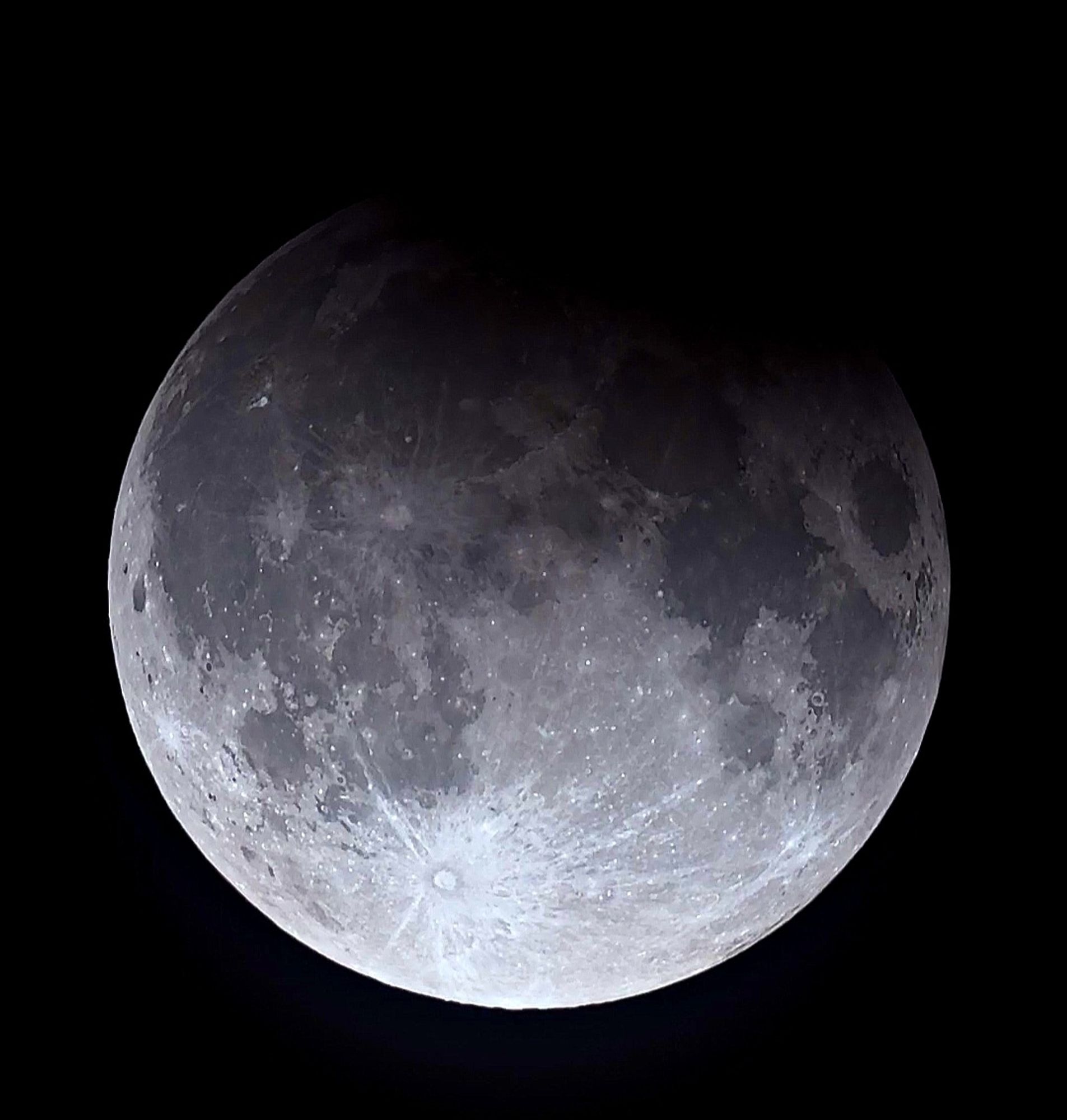 Telescope view of full moon with top quarter darkened by eclipse.