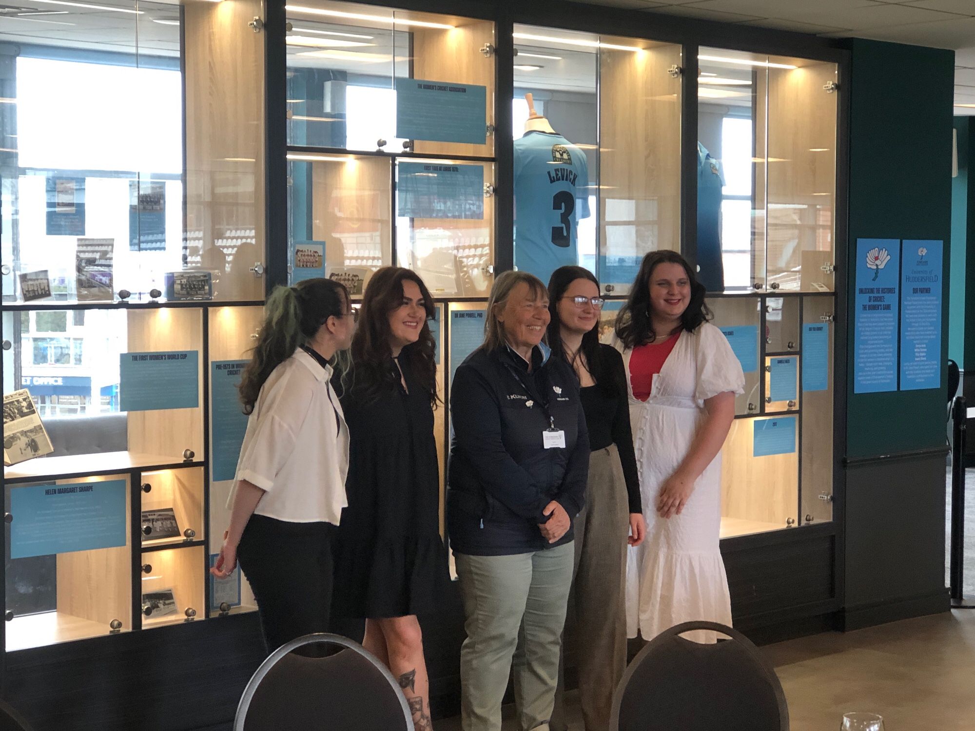 University of Huddersfield student research team stand in front of the exhibition they co-curated with the team at Yorkshire County Cricket Club. Also there is Jane Powell, former England cricketer.