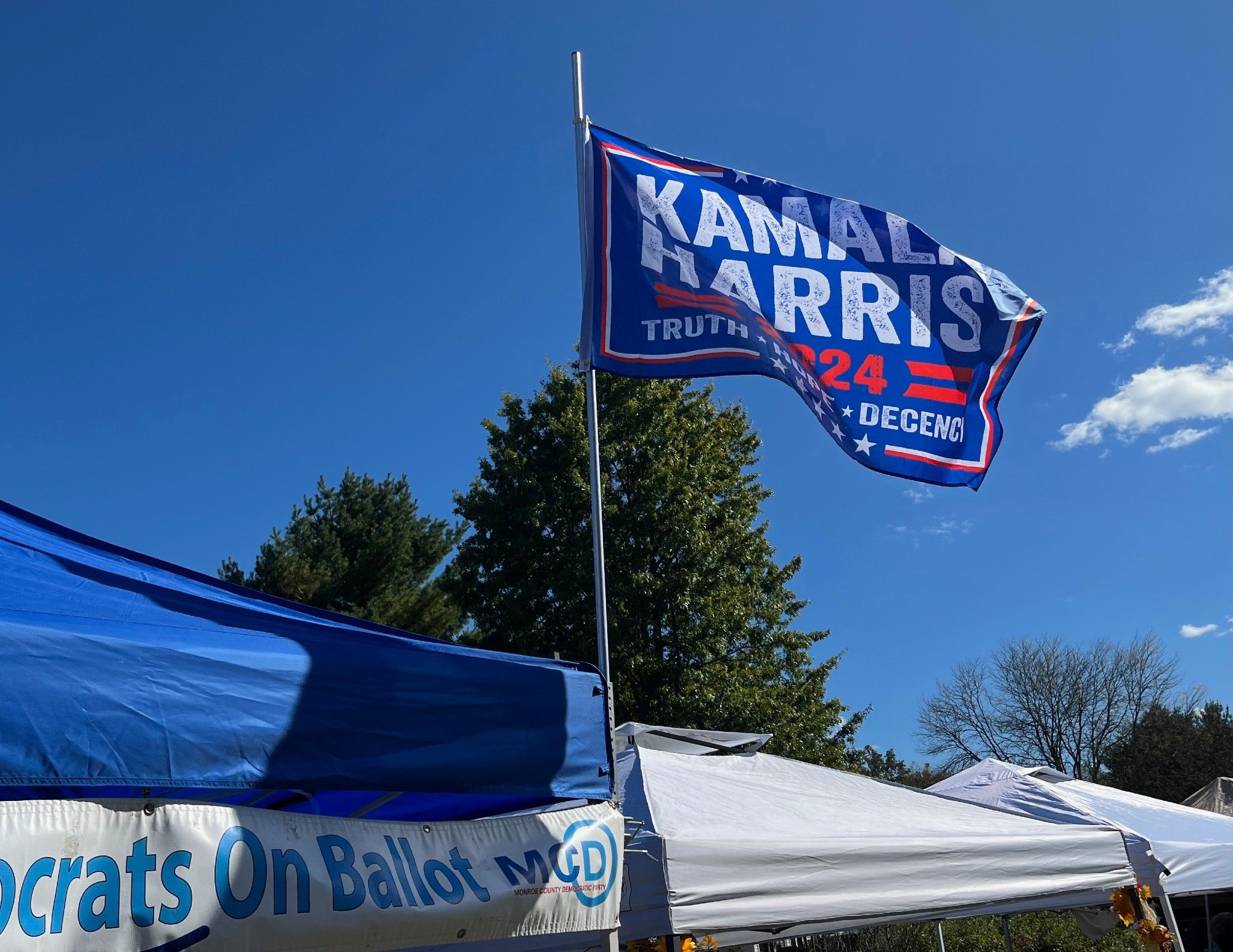 A Kamala Harris flag, designed to look like a Trump flag, flying on a canopy (the sort you'd see at an outdoor fair) that says "...crats on Ballot MCD"