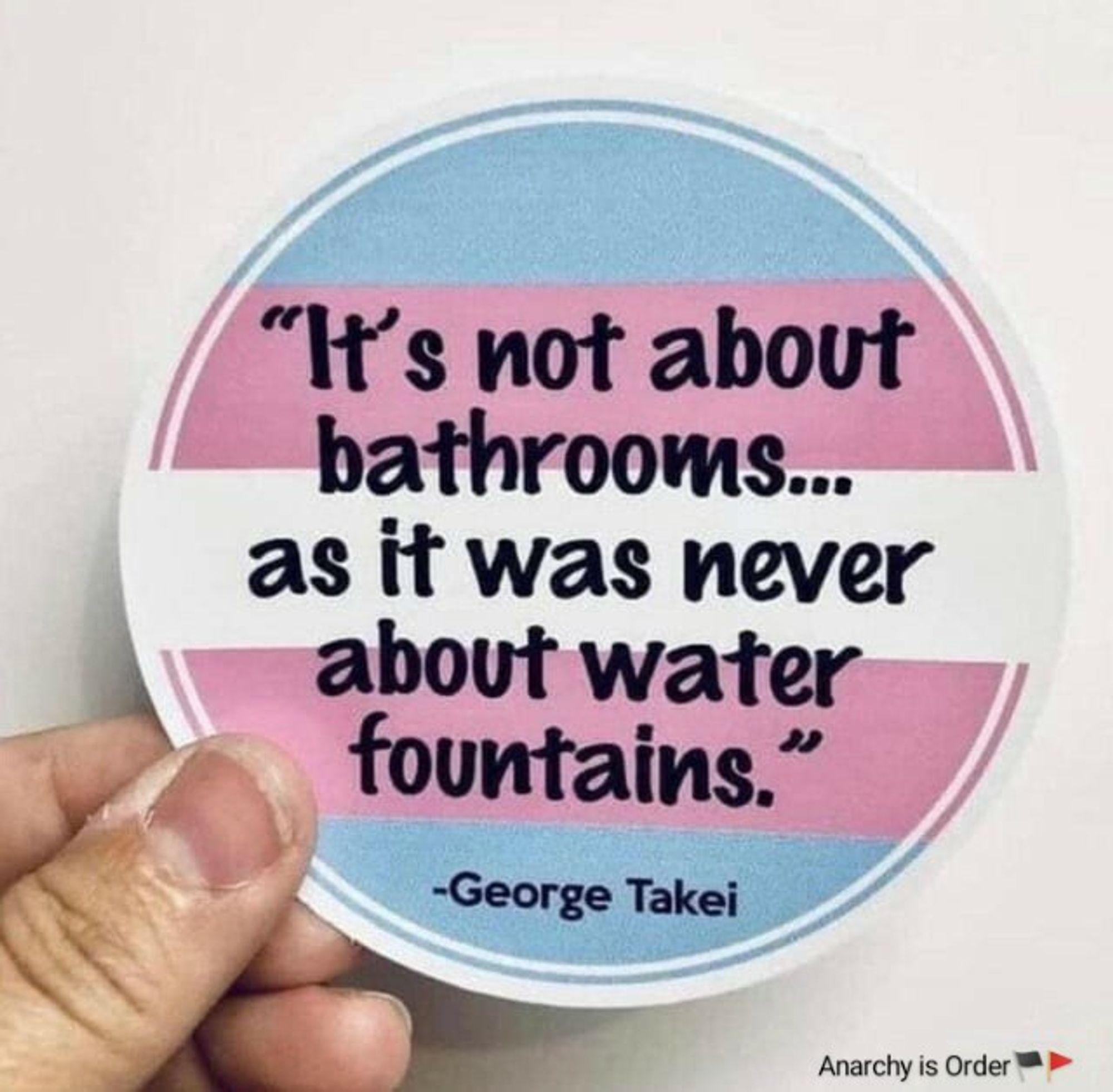 A sticker with a trans pride flag in the background with a quote from George Takei, "It's not about bathroom... as it was never about water fountains." superimposed in the foreground.