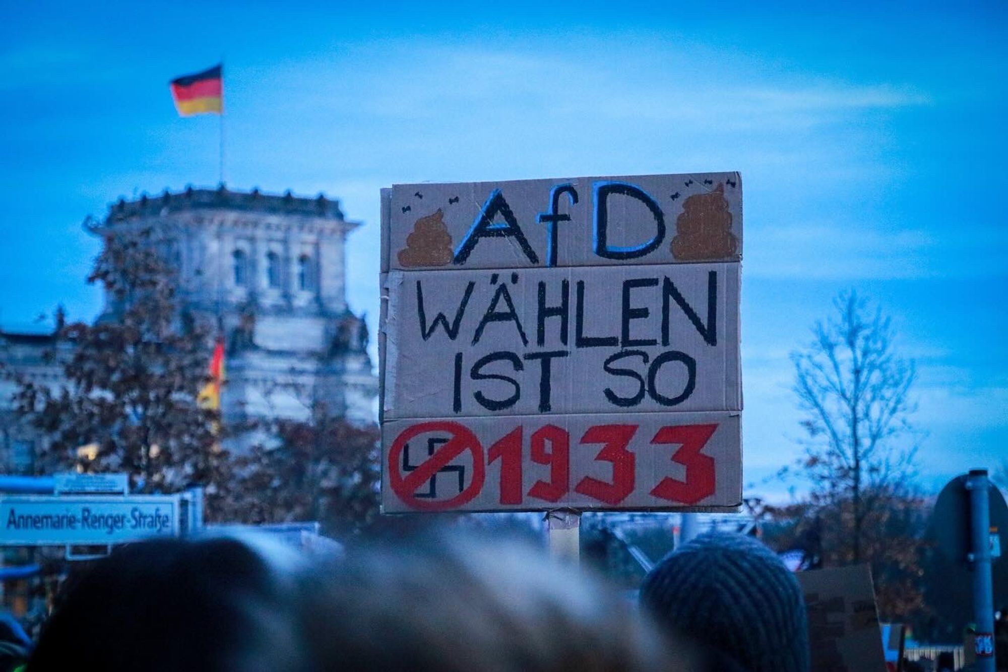 Plakat in der Menschenmenge mit der Aufschrift: "AfD Wählen ist so 1933". Im Hintergrund ist ein Turm des Reichstagsgebäudes zu sehen.