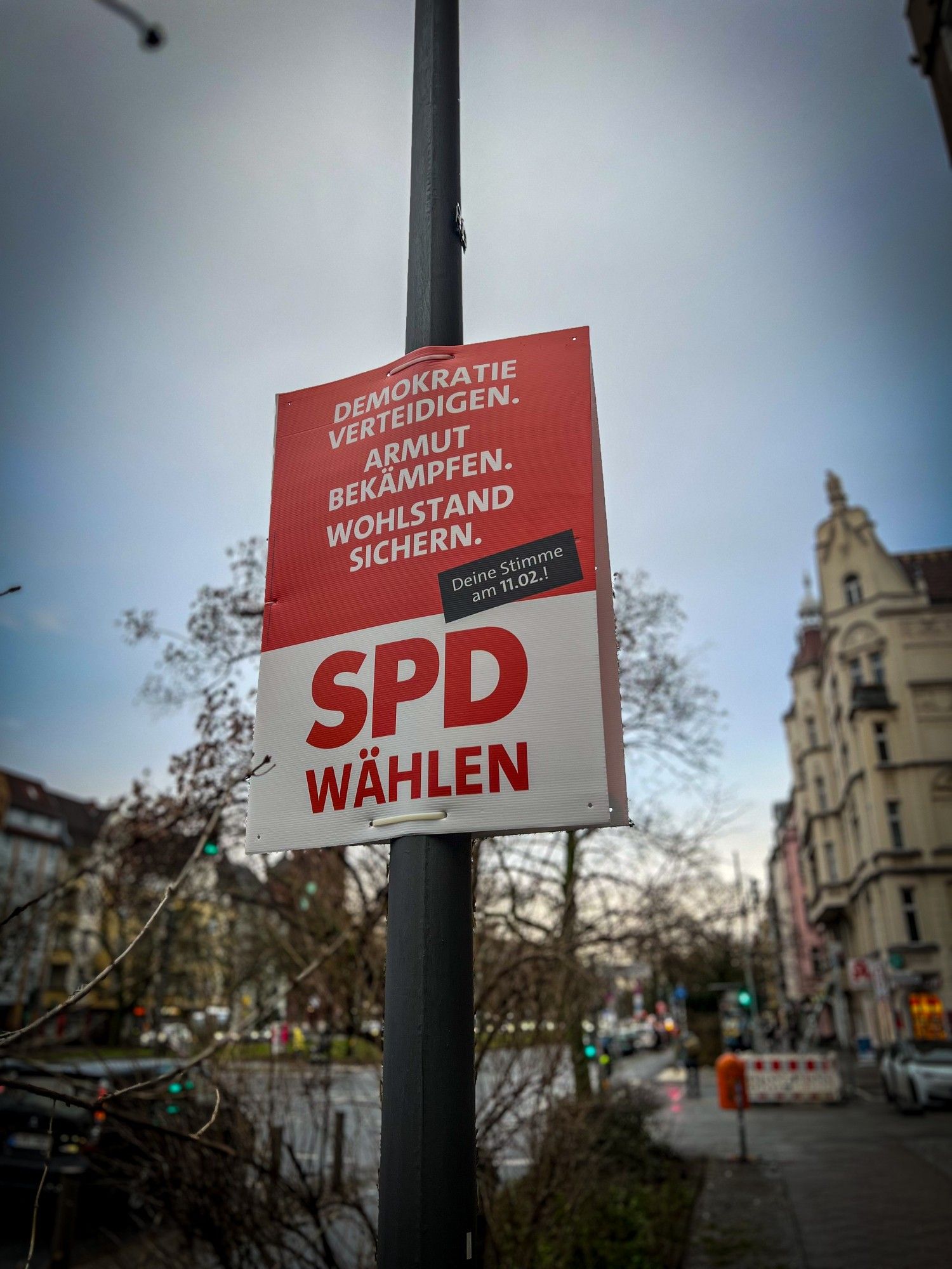 Im Vordergrund ist ein Plakat der SPD für die Wiederholungswahl am 11. Februar 2024 zu sehen. Auf dem Plakat steht oben: Demokratie verteidigen. Armut bekämpfen. Wohlstand sichern. Darunter folgt in Großbuchstaben: SPD wählen! Im Hintergrund sind Wohnhäuser entlang der Seestraße zu sehen.