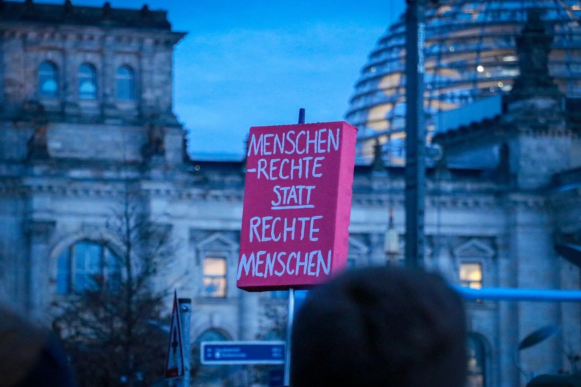 Plakat in der Menschenmenge mit der Aufschrift: "Menschenrechte statt Rechte Menschen". Im Hintergrund ist die Kuppel des Reichstagsgebäudes zu sehen.