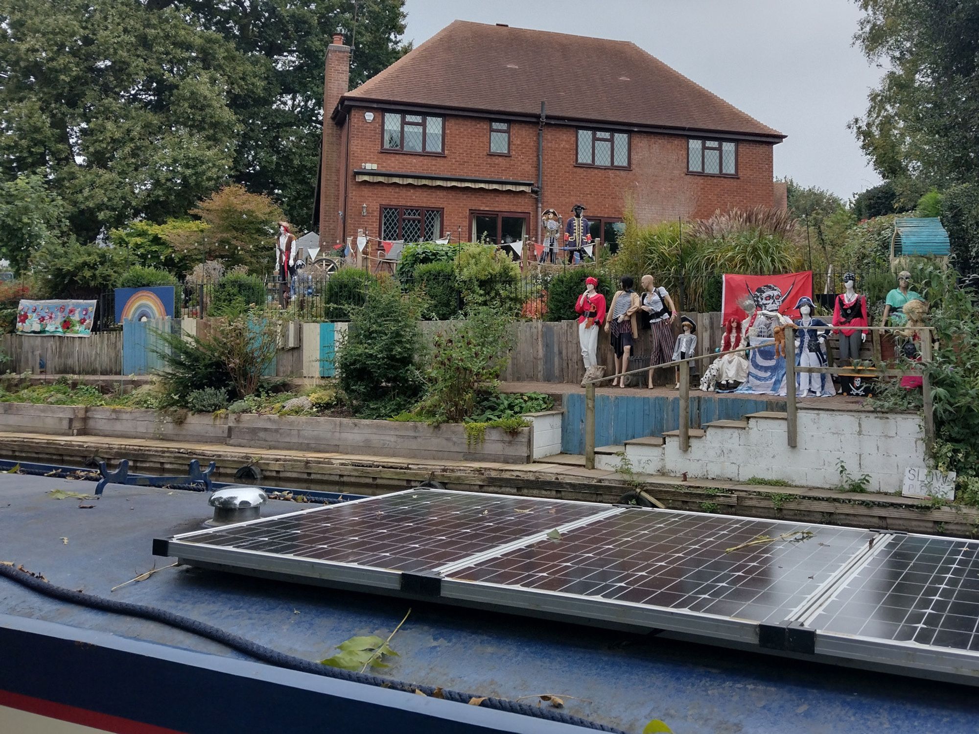 The mannequin display on the Trent & Mersey Canal in Rugeley. Today, on Talk Like A Pirate Day, the mannequins are dressed in mythical pirate outfits.
In the foreground is the blue roof of a narrowboat, with a shiny mushroom air vent, and three solar panels.