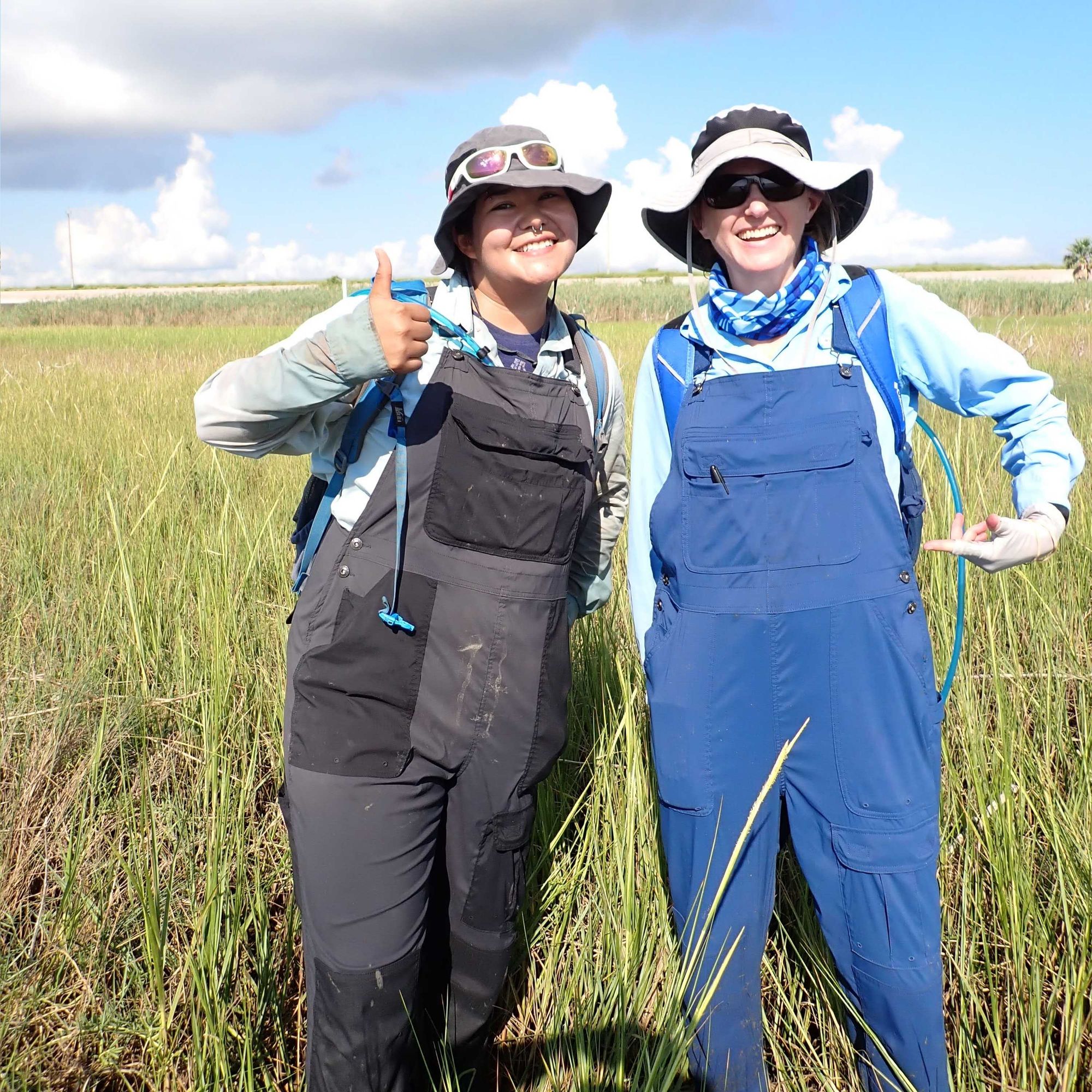 Two wetland scientists wearing overalls in the marsh