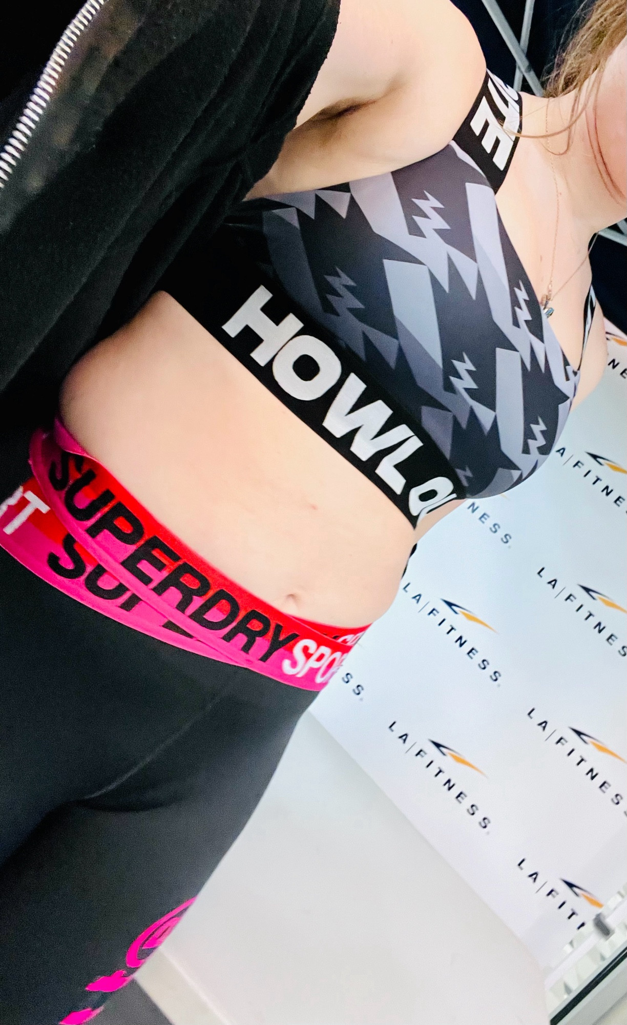 The midriff section of a woman wearing a sports bra and athletic pants with the words “ Howl Out” and “Super Dry” printed on them