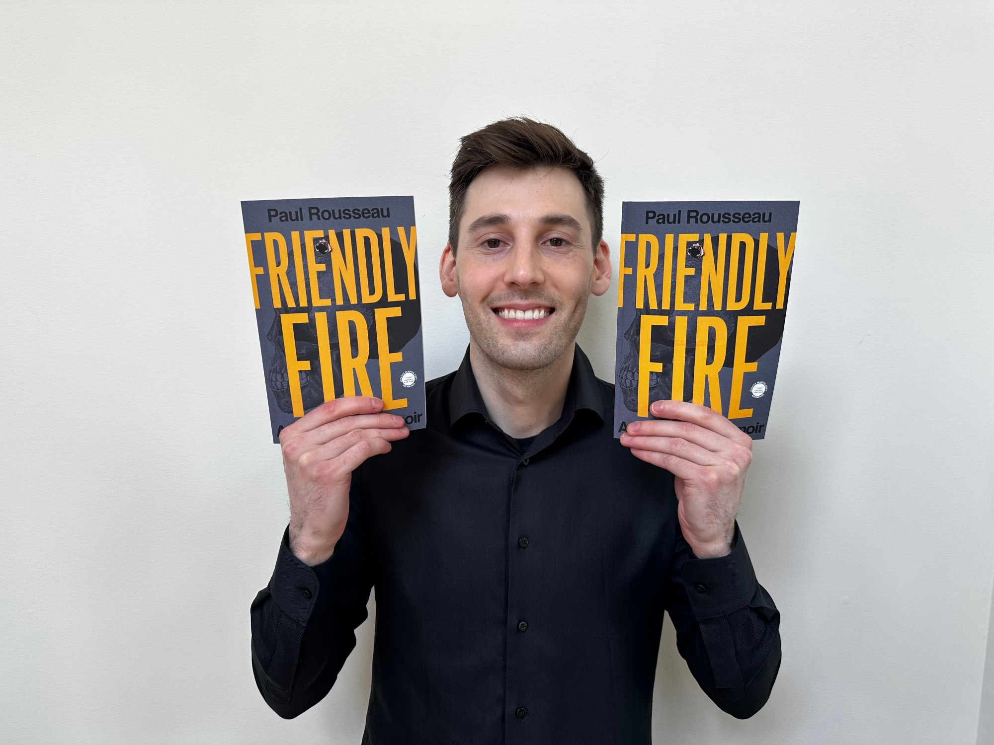 Me with 2 ARCs of friendly fire in a black button up smiling dumbly with the books held up to my face