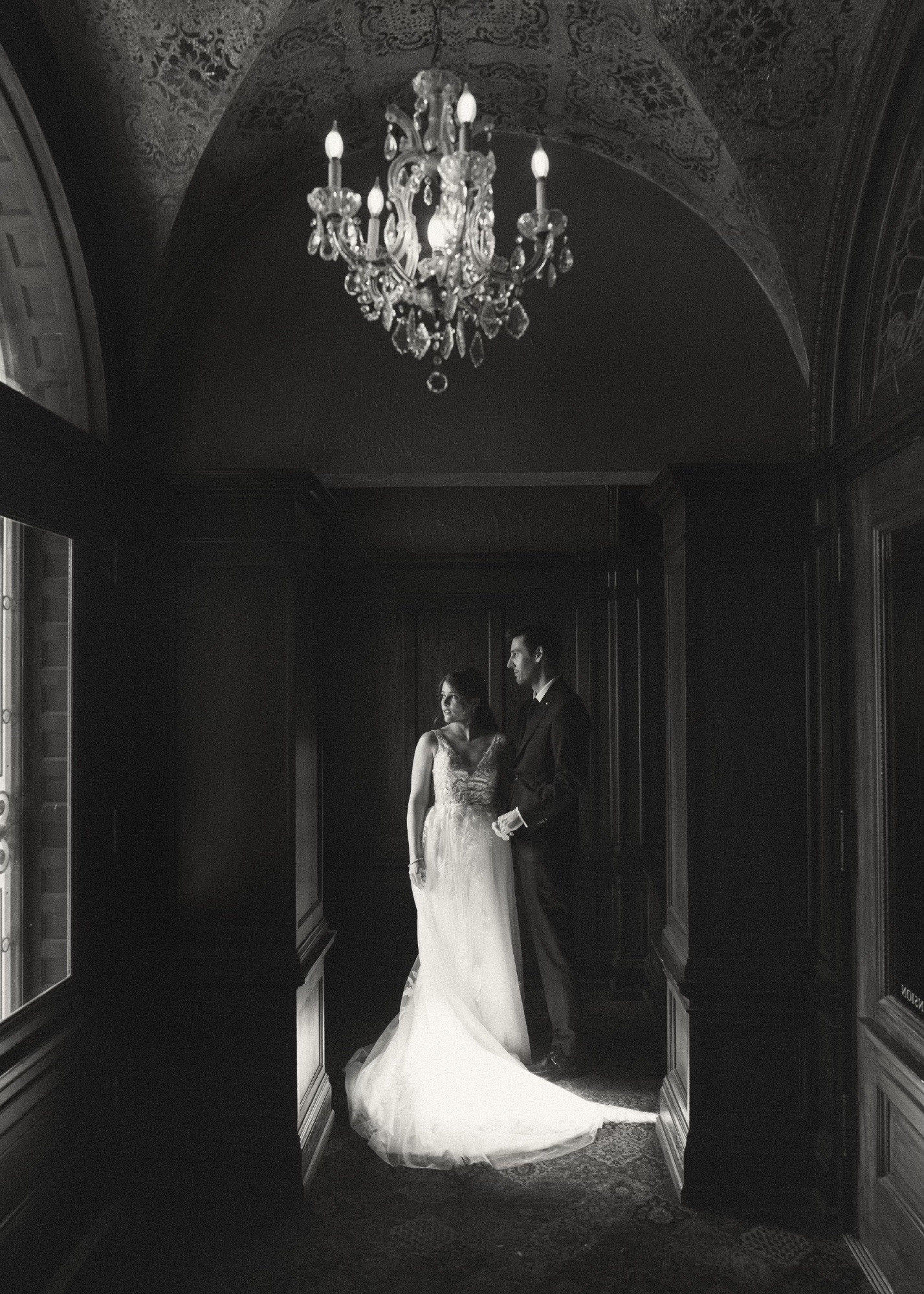 Haunted mansion wedding! Black and white photo of me and my partner in a corner of the mansion, looking longingly out a window  