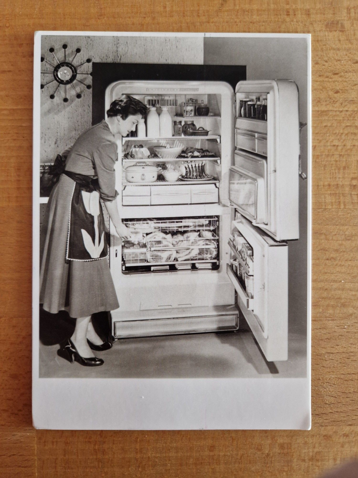 Postkarte im Stil der späten 50 Jahre. Frau in 50 Jahre Mode steht neben dem prallgefüllten Kühlschrank.