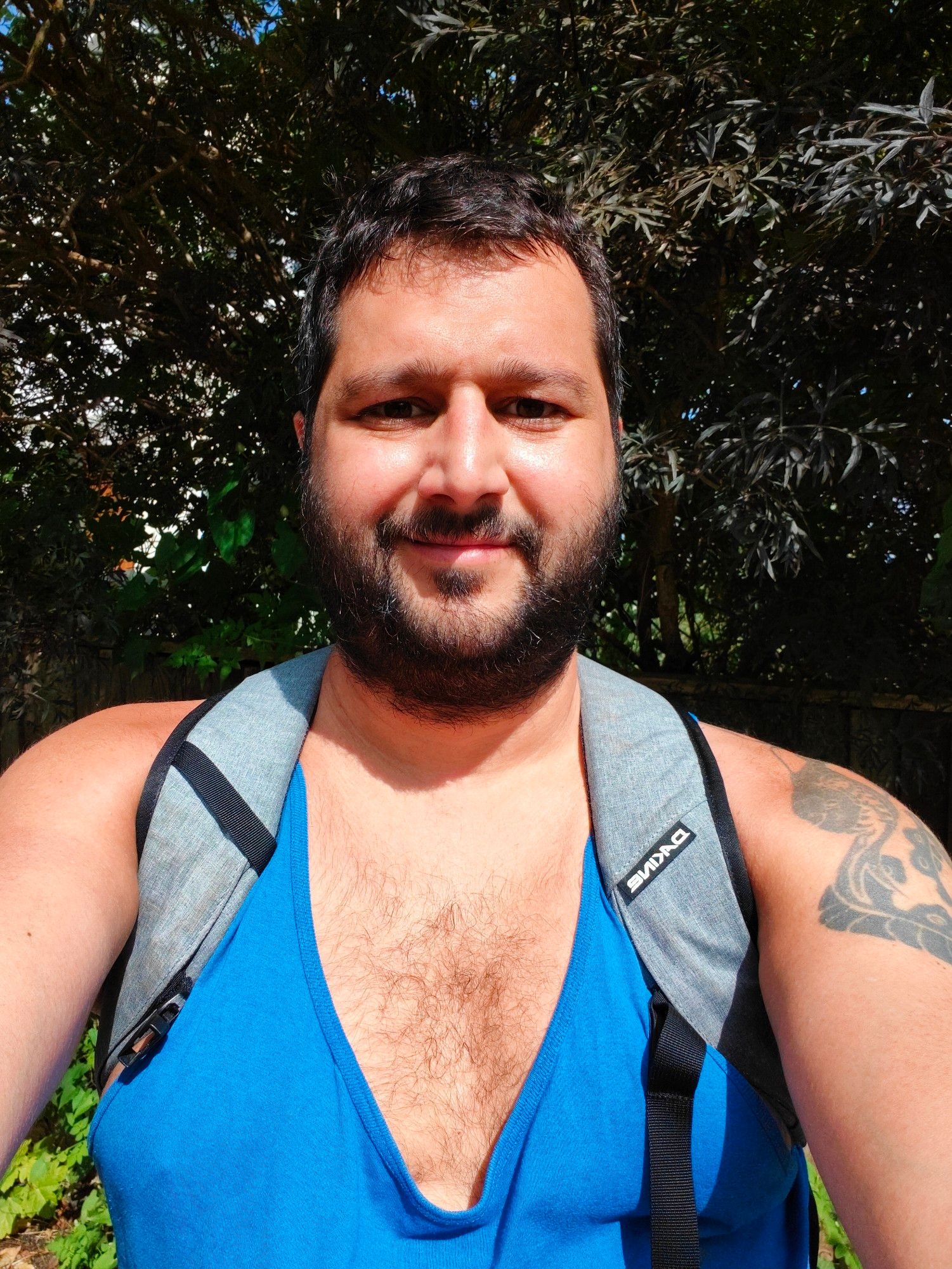 Me in a blue running vest and a grey rucksack staring into the camera with a smile on a sunny day