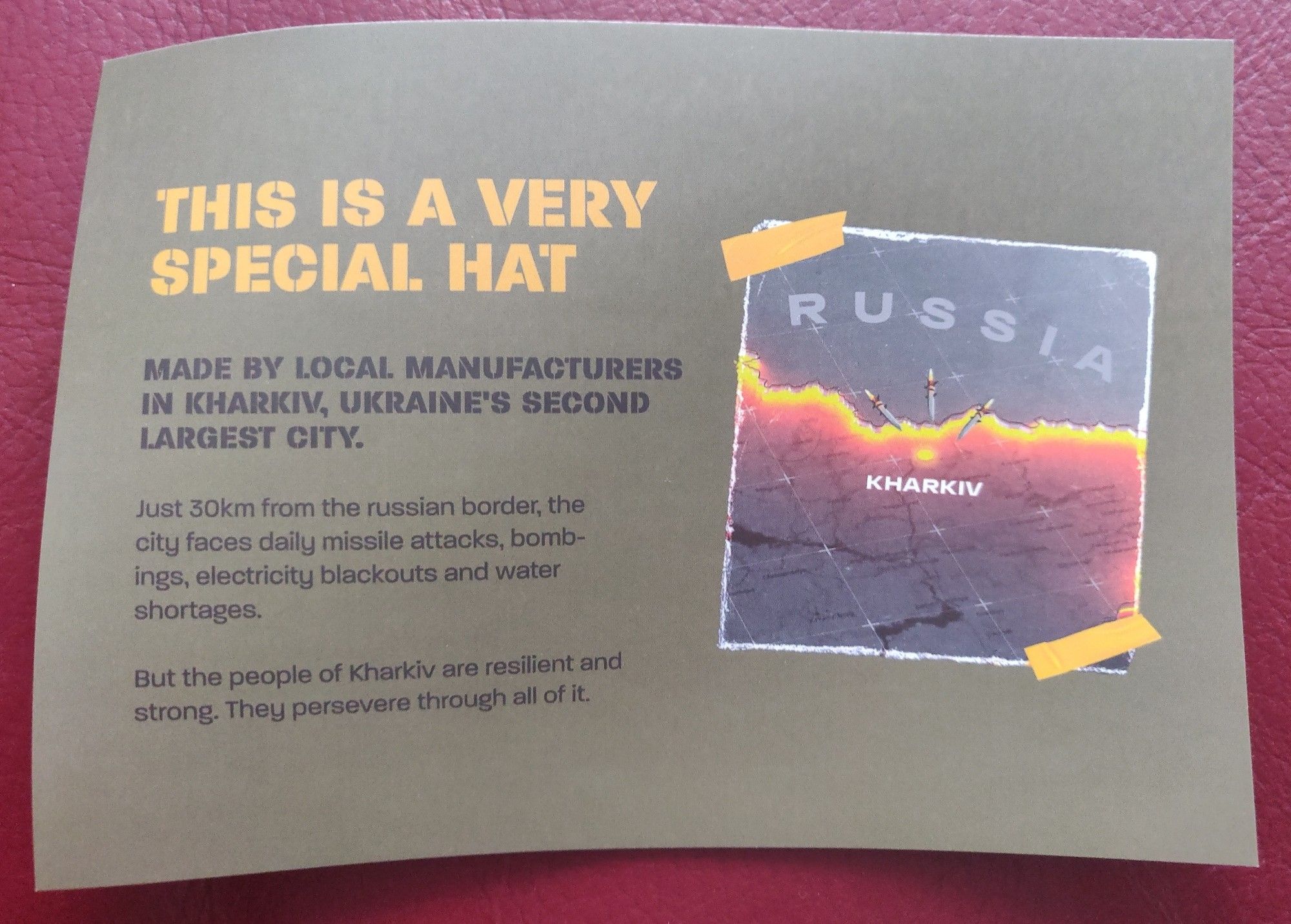 Card that reads: This is a very special hat. Made by local manufacturers in Kharkiv, Ukraine's second largest city. Just 30km from the russian border, the city faces daily missile attacks, bombings, electricity blackouts and water shortages. But the people of Kharkiv are resilient and strong. They persevere through all of it. 
The back reads: This hat is a small symbol of support for them, and you should wear it proudly so you help tell their story to your friends, families and neighbours.