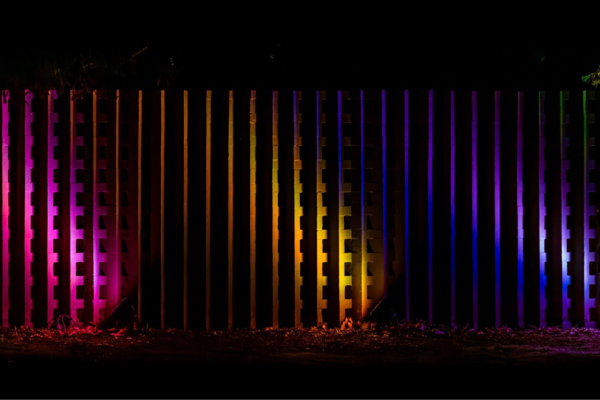 Eine bunt beleuchtete Mauer bei Nacht.
Die Mauer ist nicht glatt. Schräge Elemente und Kassetten sind zu sehen.