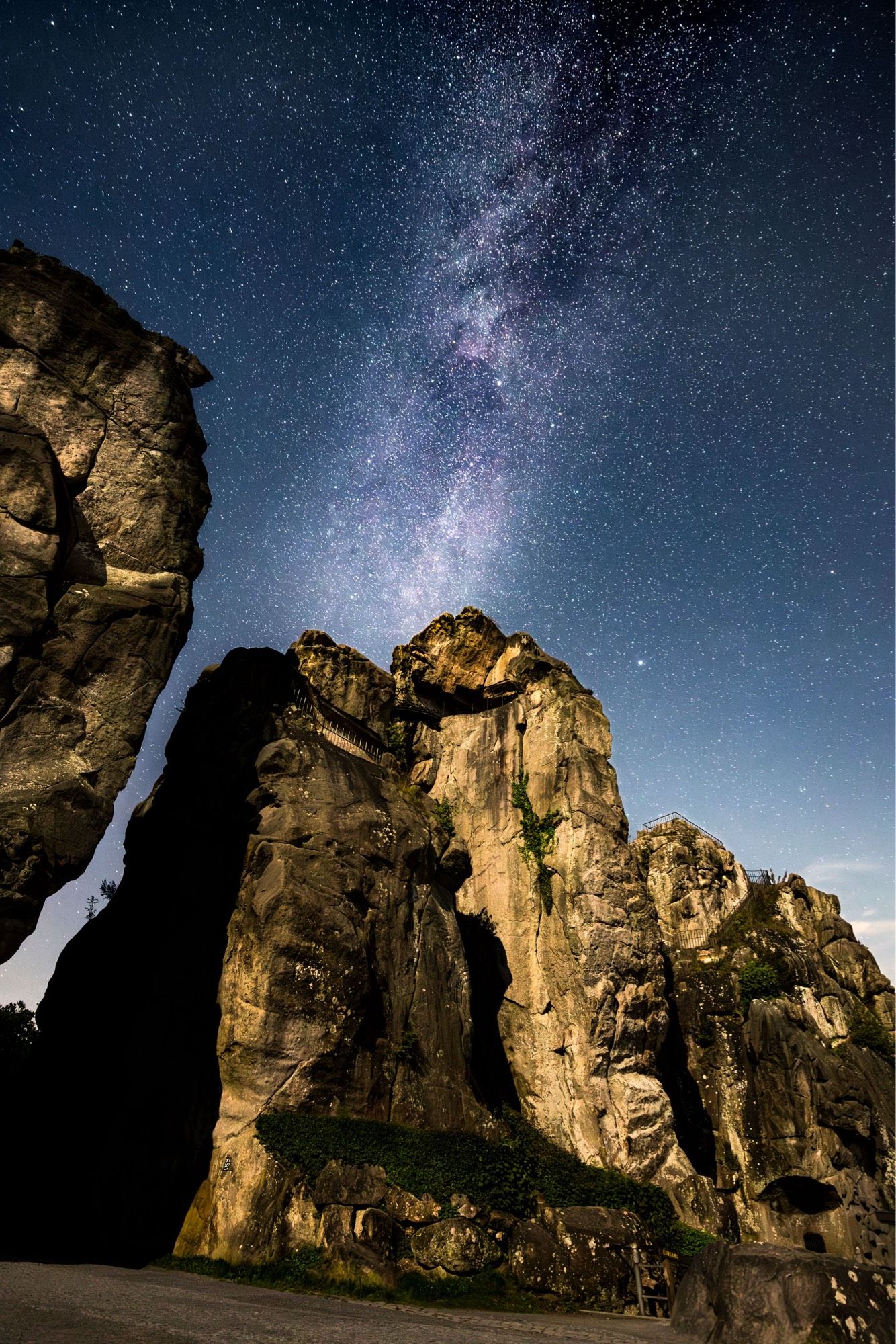 Die Felsformation der Externsteine bei Nacht. Im sommerlichen Nachthimmel strahlt darüber das Band unserer Heimatgalaxie, der Milchstraße.