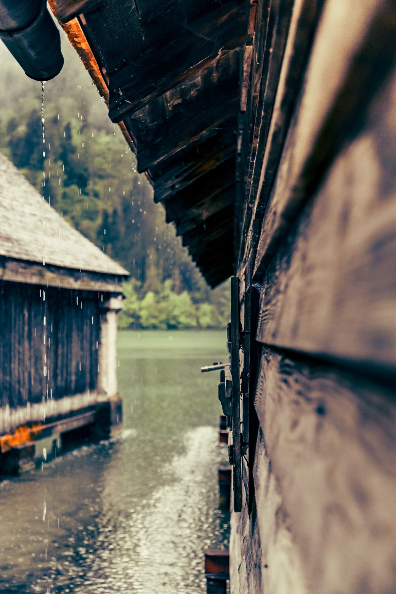 Nahaufnahme von Bootshäusern am Rande eines Sees. Regenwasser tropft von der Regenrinne