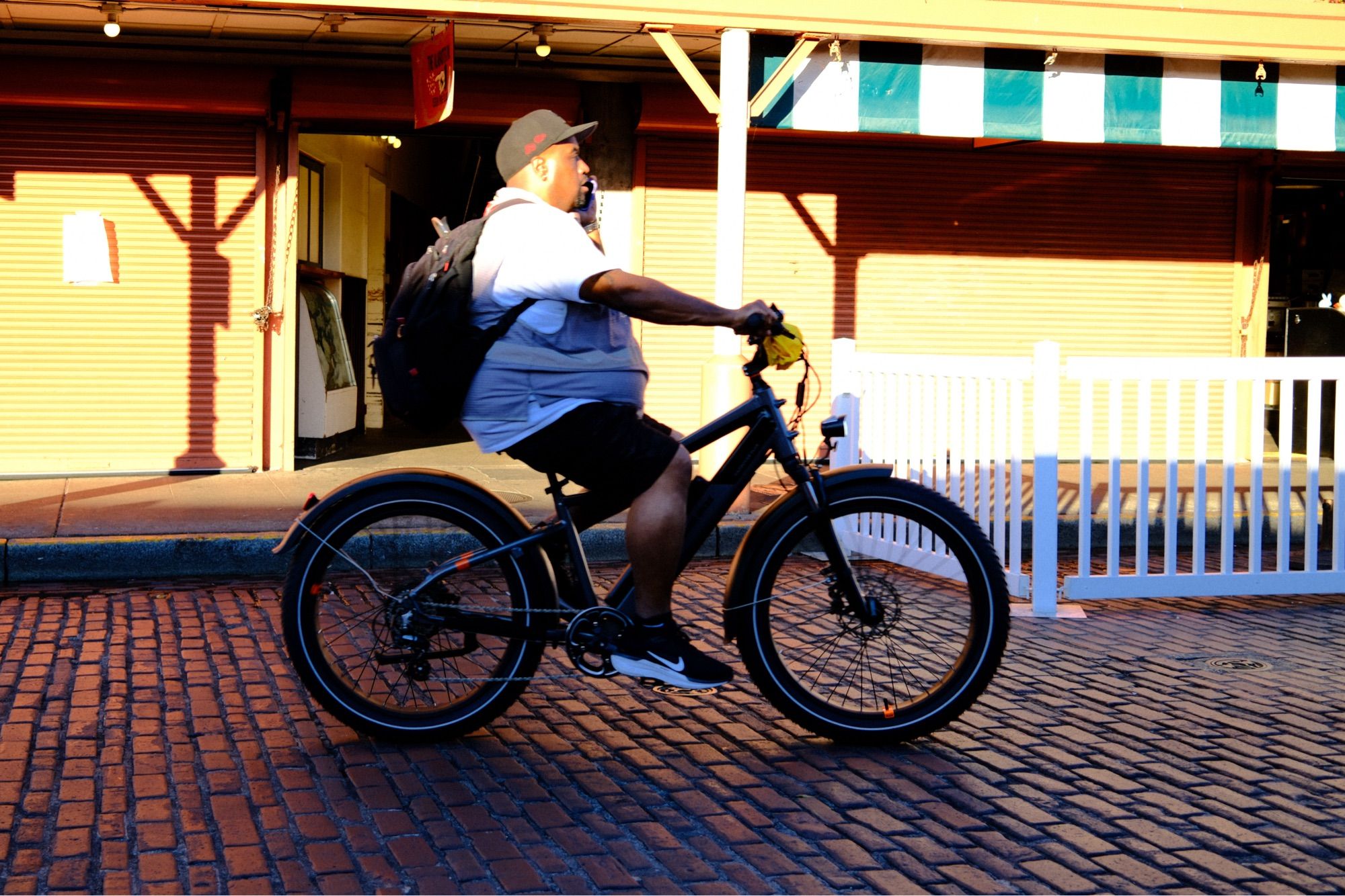 A man riding a bicycle along a brick road. The sun is lighting up the top half of the man’s head