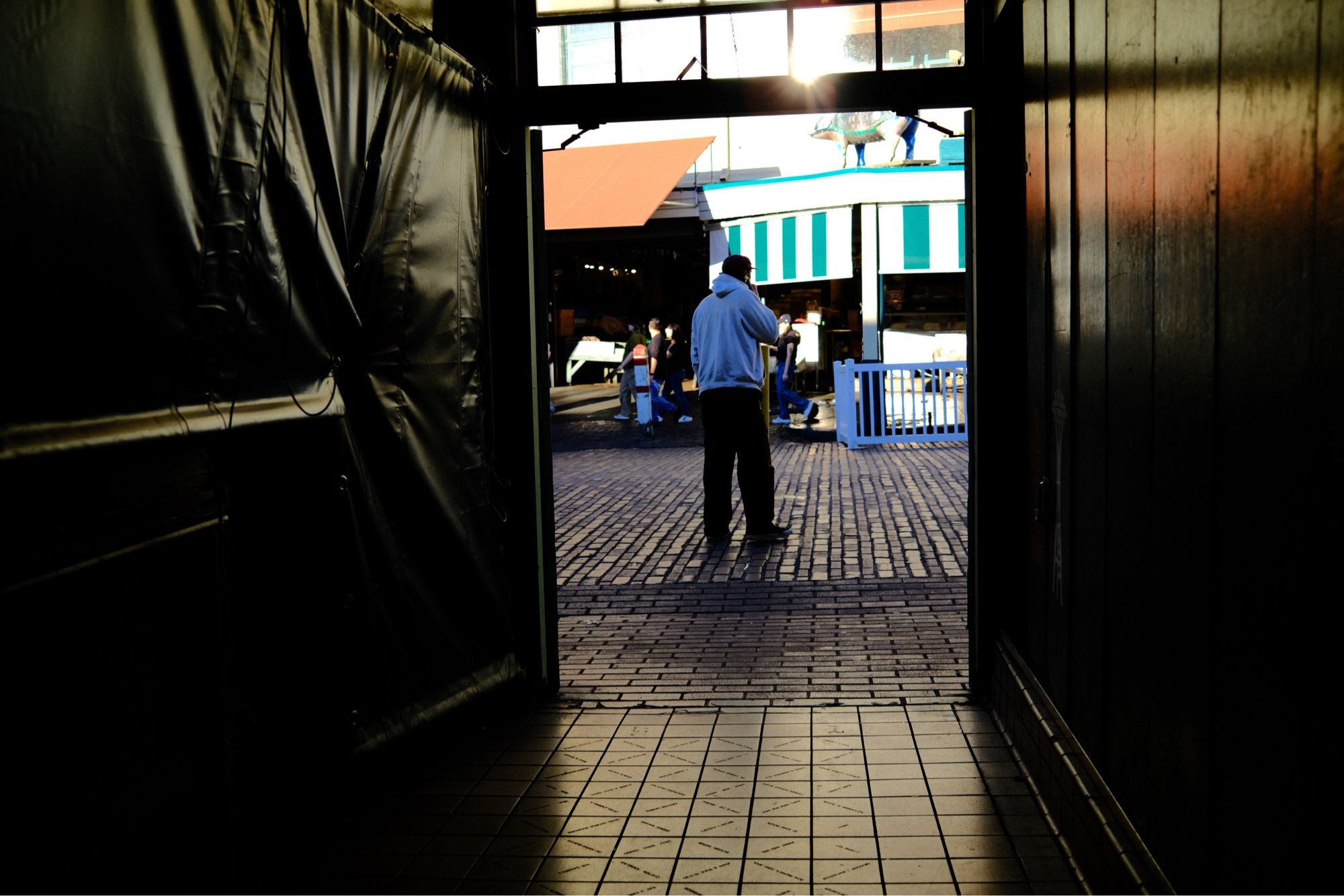 A short hallway to an open door with a man standing outside in a street market.