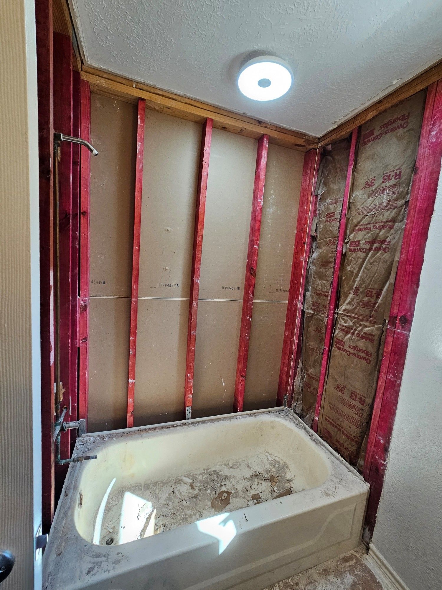 A bath/shower with all the walls ripped out and debris everywhere