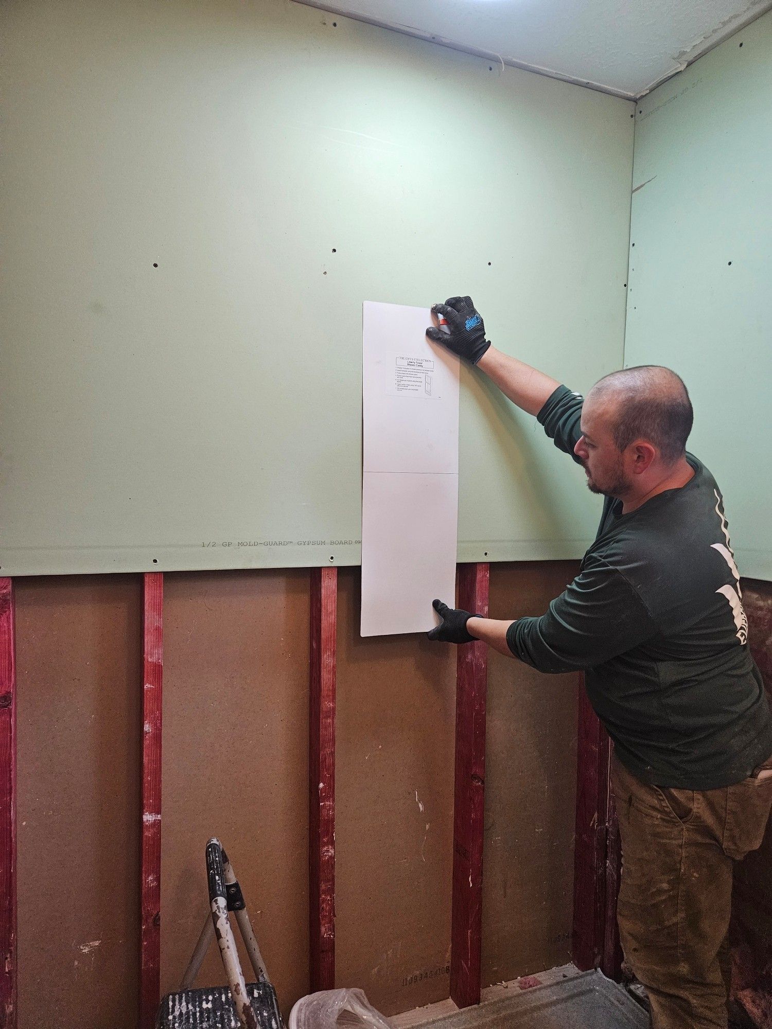 Construction guy holding a paper cut out of soaps holder up to the wall to judge placement