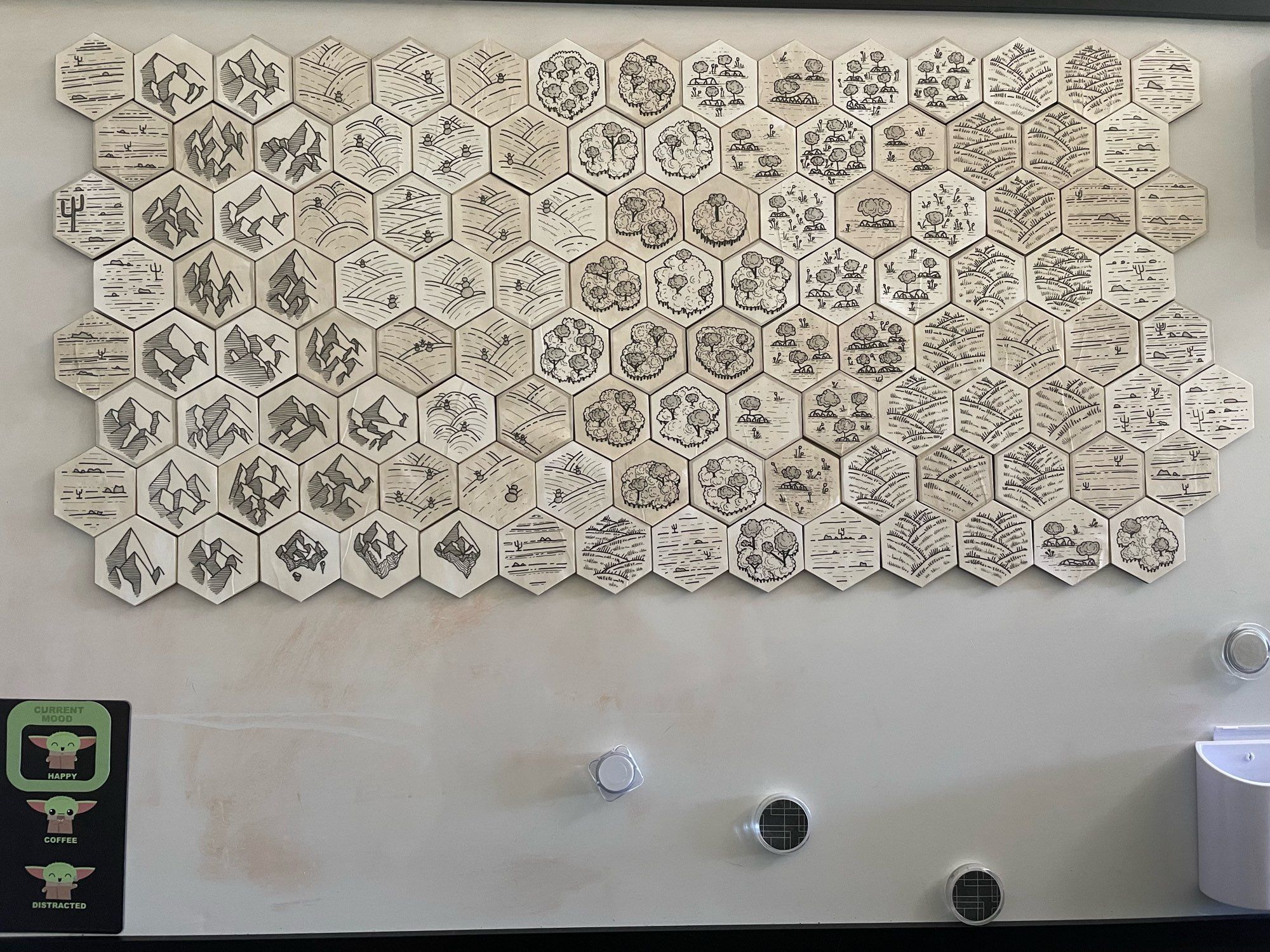 116 hexes of varying aged paper color stuck to a whiteboard. It has desert tiles, mountains, floating mountains, arctic, forest, wetland, and grassland illustrations.