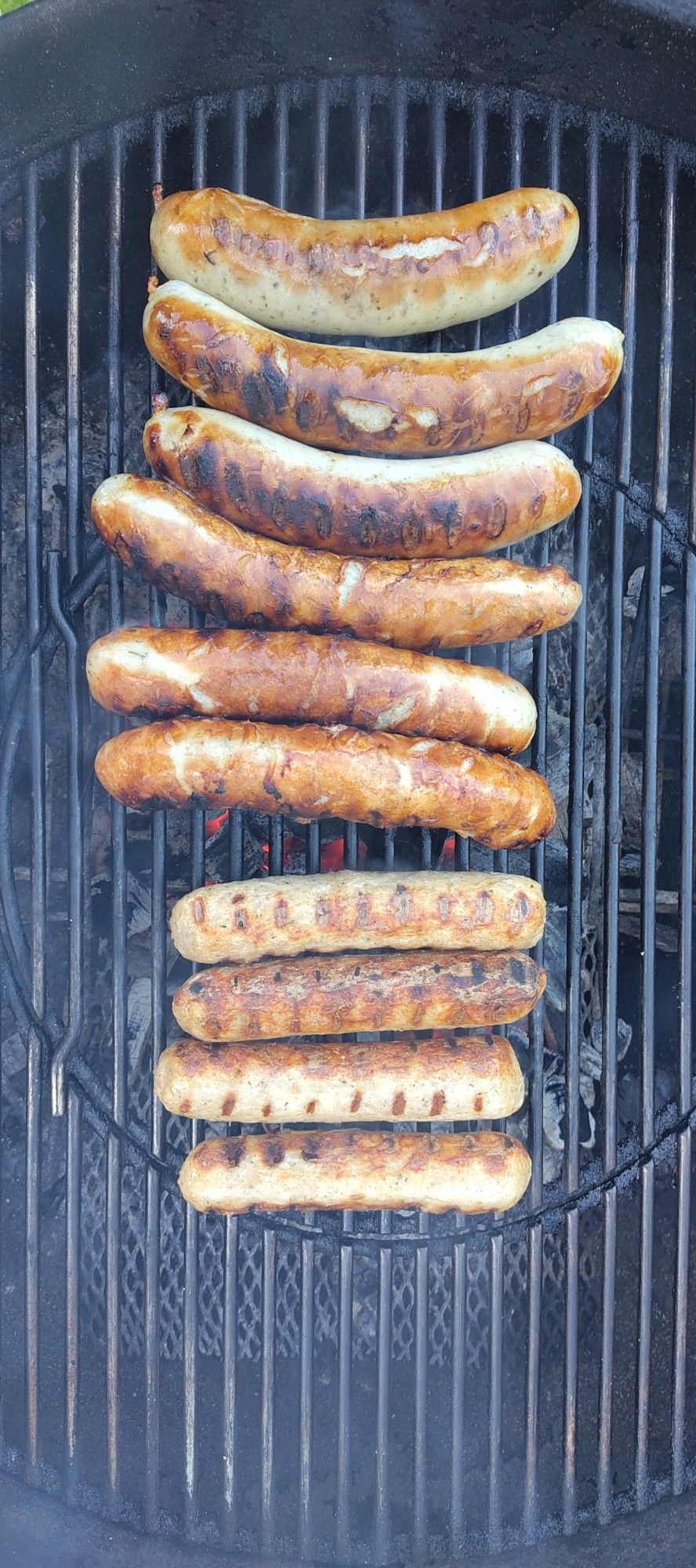 Nicht vegetarische (oben) und vegetarische (unten) Würstchen auf dem Rost eines Holzkohlegrills