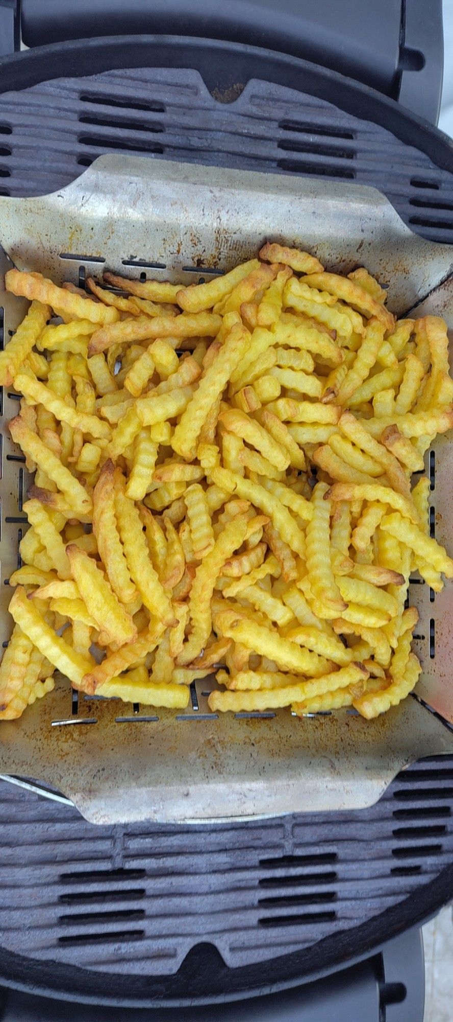 Pommes Frittes im Gemüsekorb auf dem Rost eines Gasgrills