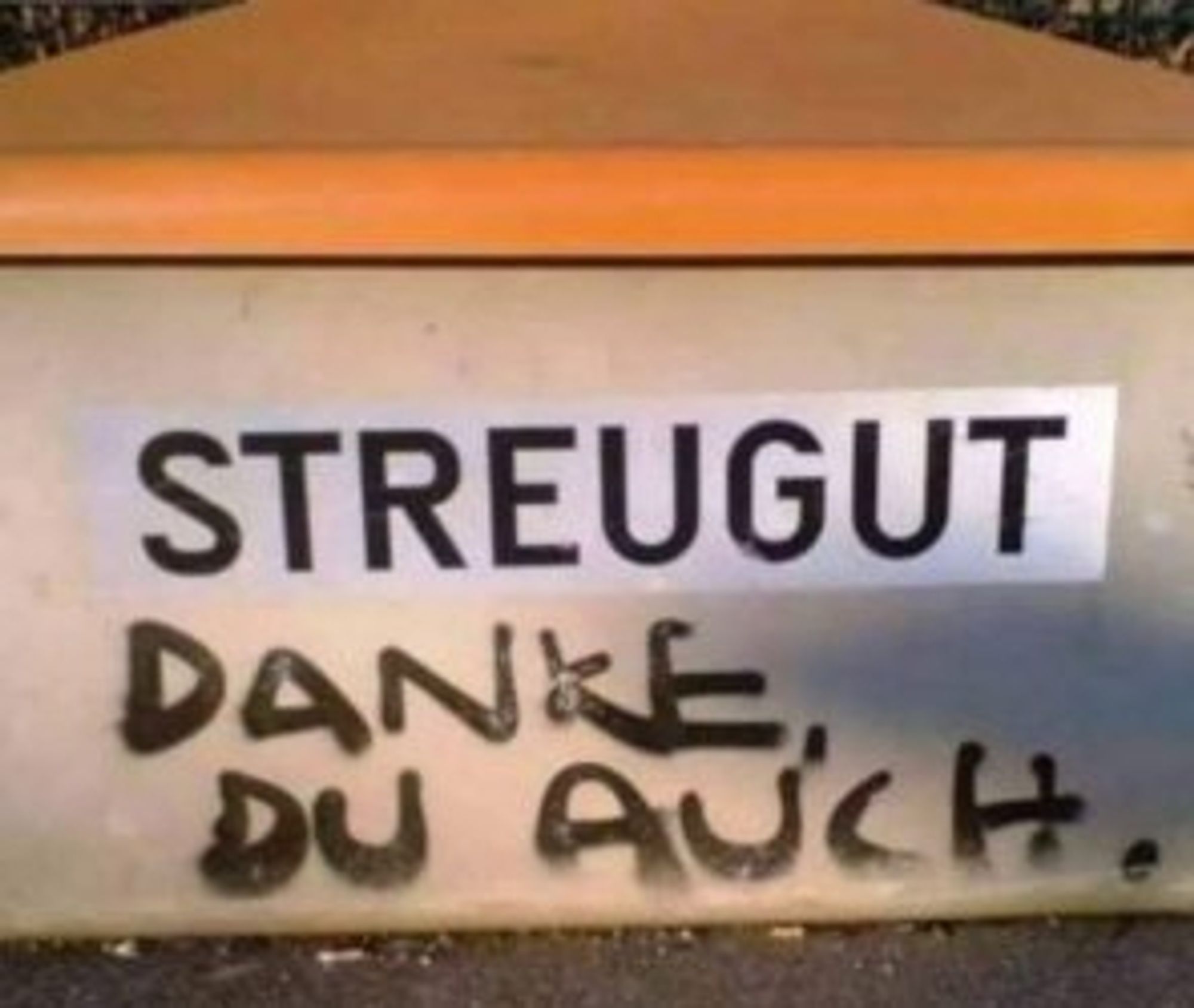 Das Bild zeigt eine gelbe Oberfläche mit dem Wort “STREUGUT” darauf gedruckt. Unter dem gedruckten Text steht handschriftlich “DANKE DU AUCH.” in Schwarz.