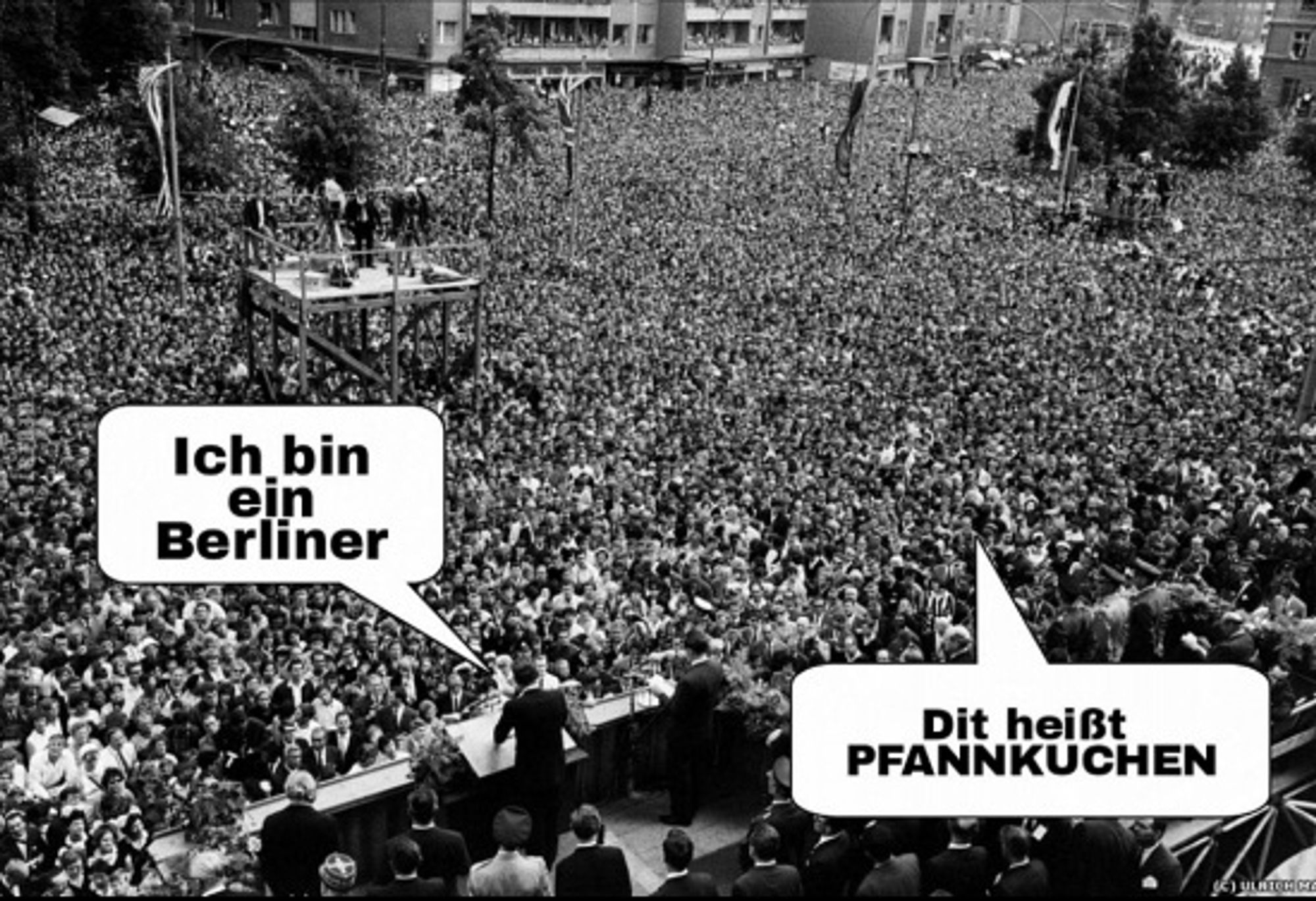 Das Bild zeigt eine große Menschenmenge, die sich um ein Podium versammelt hat. Es gibt zwei Sprechblasen mit Text auf Deutsch. Die erste Sprechblase sagt “Ich bin ein Berliner”, was “I am a Berliner” bedeutet. Die zweite Sprechblase liest “Dit heißt PFANNKUCHEN”, was “Das bedeutet PFANNKUCHEN” bedeutet. Dieses Bild ist interessant, da es auf den berühmten Satz des US-Präsidenten John F. Kennedy während seiner Rede 1963 in West-Berlin anspielt, der dazu gedacht war, Solidarität mit den Menschen in Berlin während des Kalten Krieges zu zeigen. Es gibt jedoch eine urbane Legende, dass “Berliner” auch auf eine Art Gelee-Donut hinweist, was zu humorvollen Fehlinterpretationen führt, wie sie durch die zweite Sprechblase angedeutet wird.