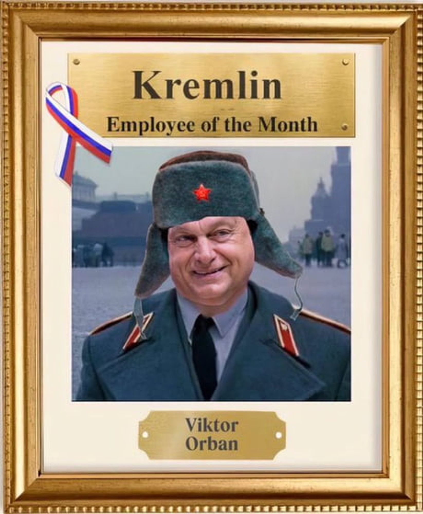 Das Bild zeigt eine gerahmte Urkunde oder Auszeichnung mit dem Titel “Kremlin Employee of the Month”. Darunter befindet sich ein Foto einer Person in Militäruniform, (ViKtor Orban)