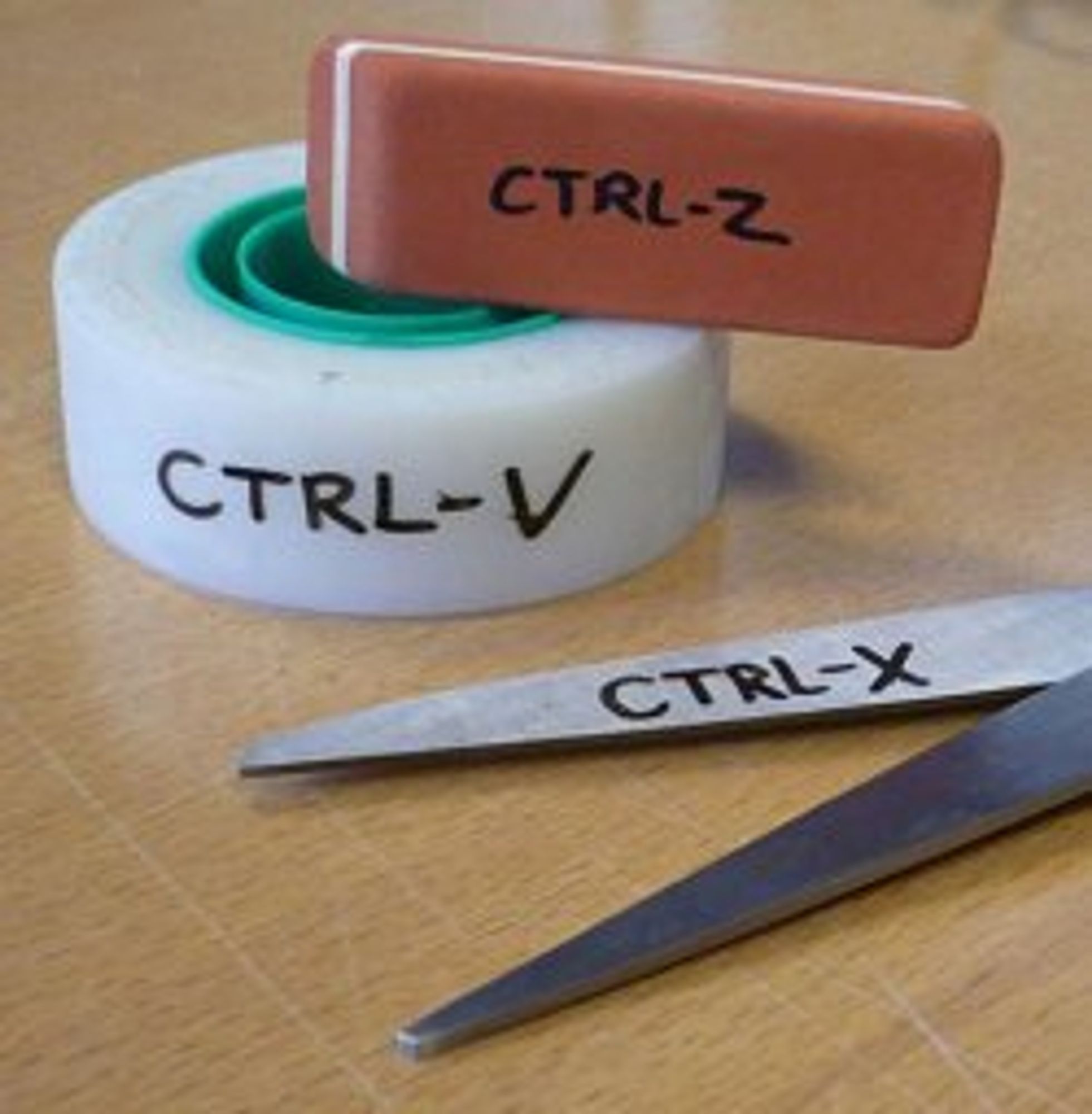 Das Bild zeigt drei Objekte, die jeweils mit einem Tastaturkürzel beschriftet sind. Es gibt eine Rolle Klebeband, die mit “CTRL-V” beschriftet ist, was die ‘Einfügen’-Funktion darstellt. Ein rosa Radiergummi ist mit “CTRL-Z” beschriftet und symbolisiert die ‘Rückgängig’-Funktion. Schließlich gibt es eine Schere , die mit “CTRL-X” beschriftet ist, was die ‘Ausschneiden’-Funktion anzeigt. Dieses Bild ist interessant, da es Computertastaturbefehle kreativ mit physischen Objekten darstellt, die im realen Leben ähnliche Funktionen haben: Kleben für Einfügen, Radieren für Rückgängigmachen und Schneiden für Ausschneiden.