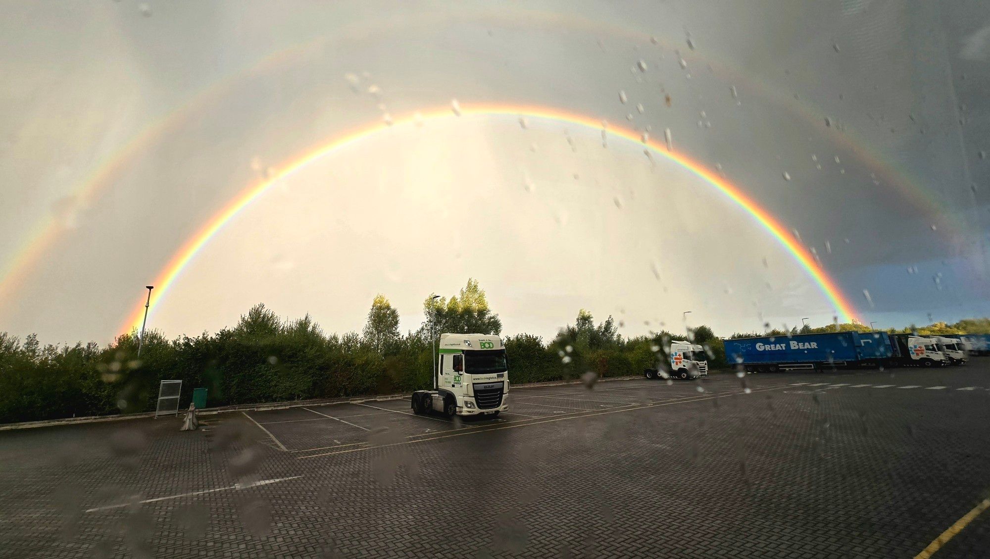 Double rainbow in truck yard. A couple of truck units and a few trailers.