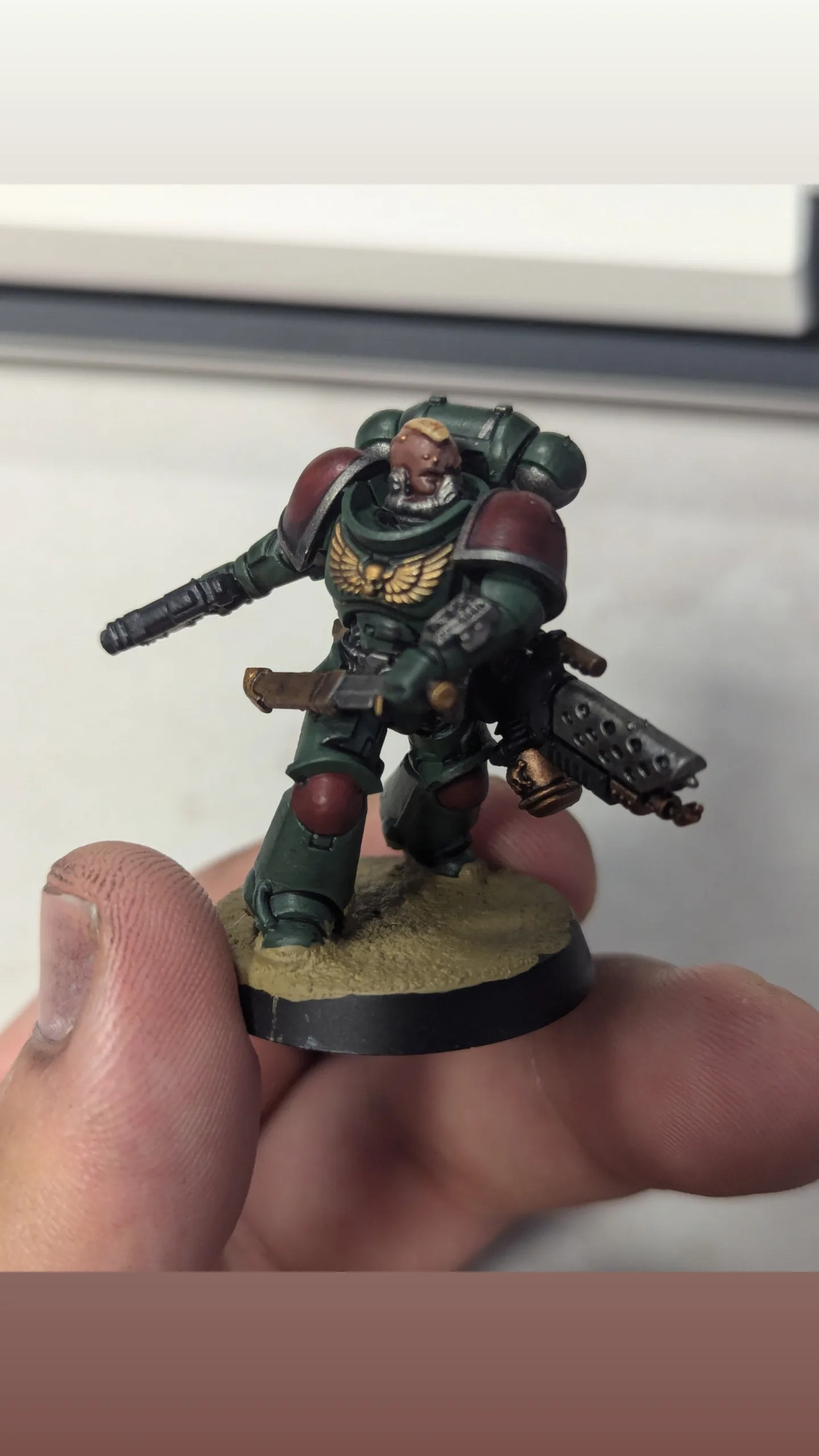 A space marine mini drawing a combat knife lunging forward, painted in green and red with metallic silver and gold accents on a desert sand base