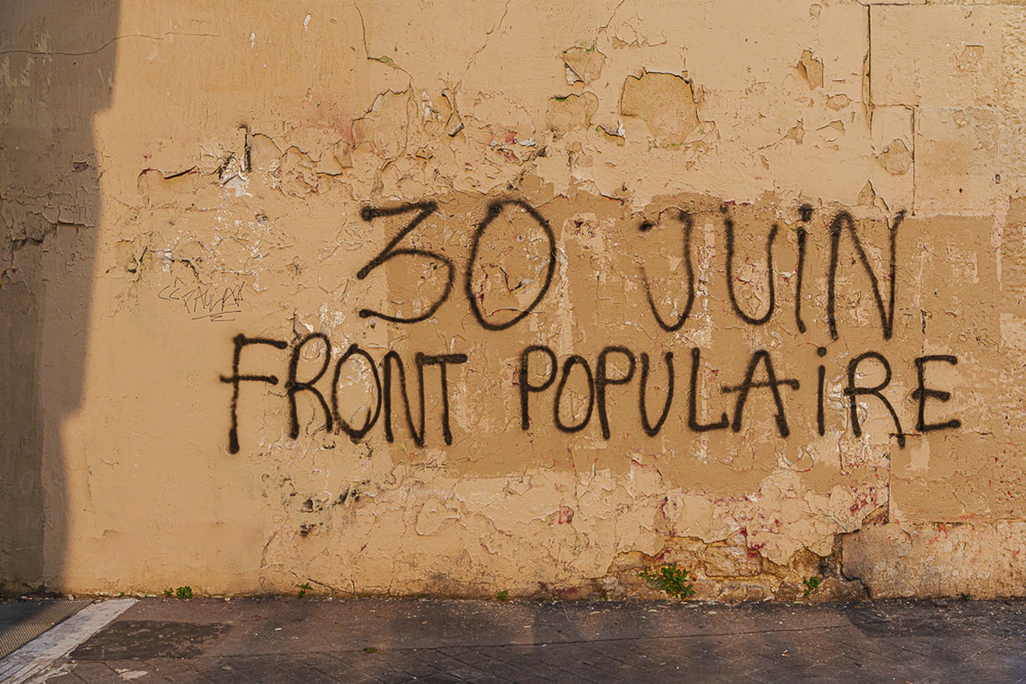 "30 juin FRONT POPULAIRE" écrit en noir sur un mur parisien éclairé par le soleil