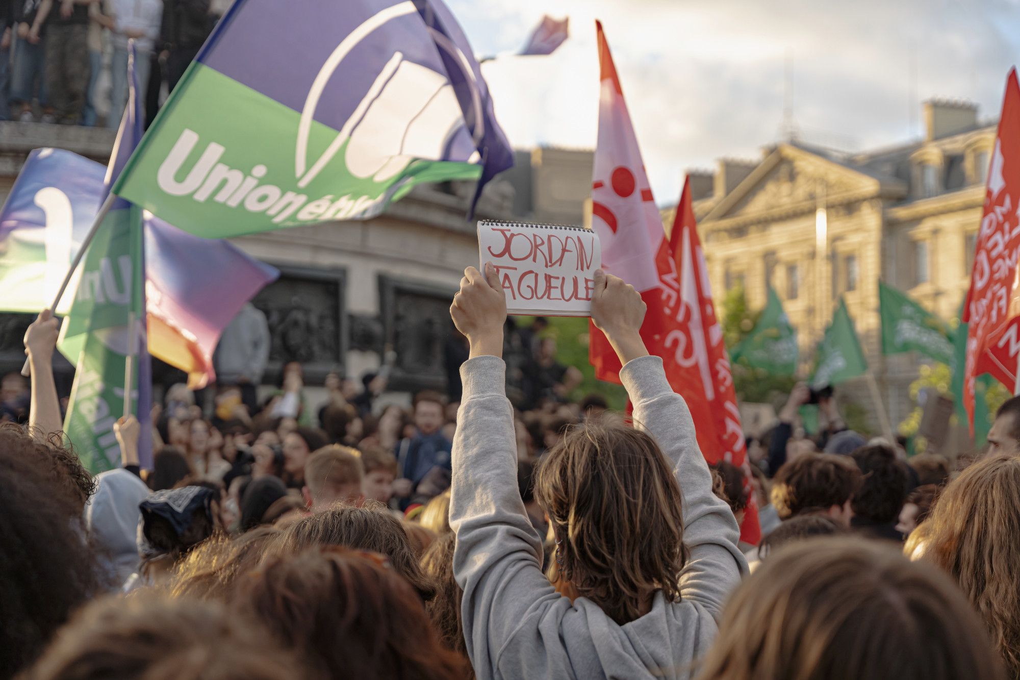 Au milieu de drapeaux, un ou une manifestant-e fait face à Marianne, place de la République, et tient à bout de bras, entre ses mains cette pancarte "Jordan ta gueule"