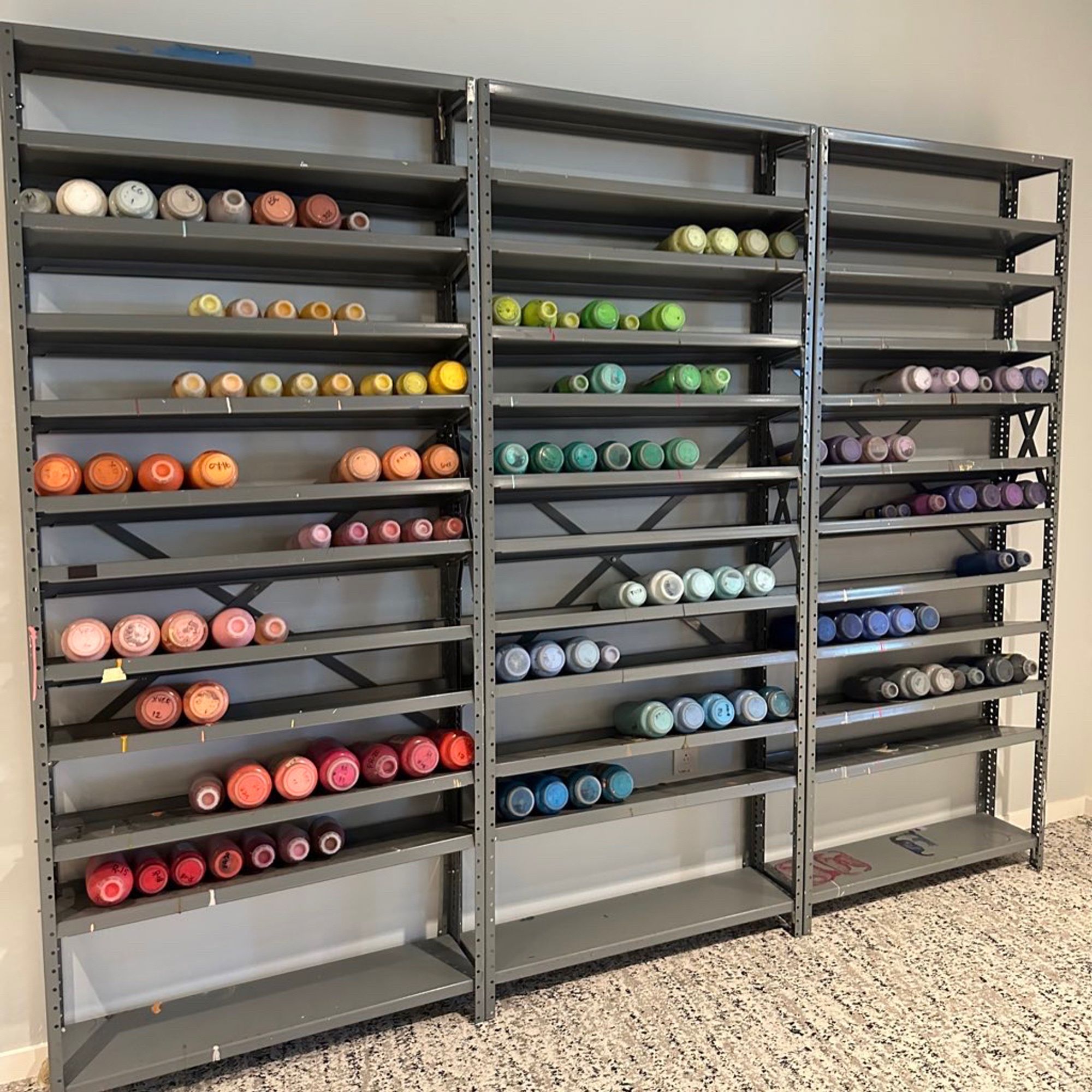 Bookshelves of big bottles of paint, stacked in rainbow color order. Paint previously used for making traditionally animated cartoons.