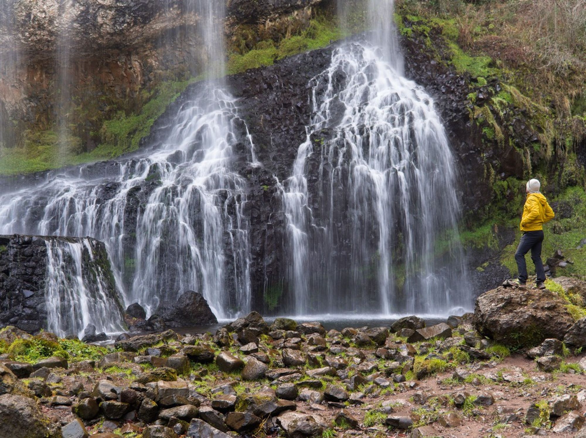 homme en jaune qui pose au pied de la cascade de la Beaume. La photo est prise en pose longue pour donner un effet de filé à l'eau qui ruisselle.