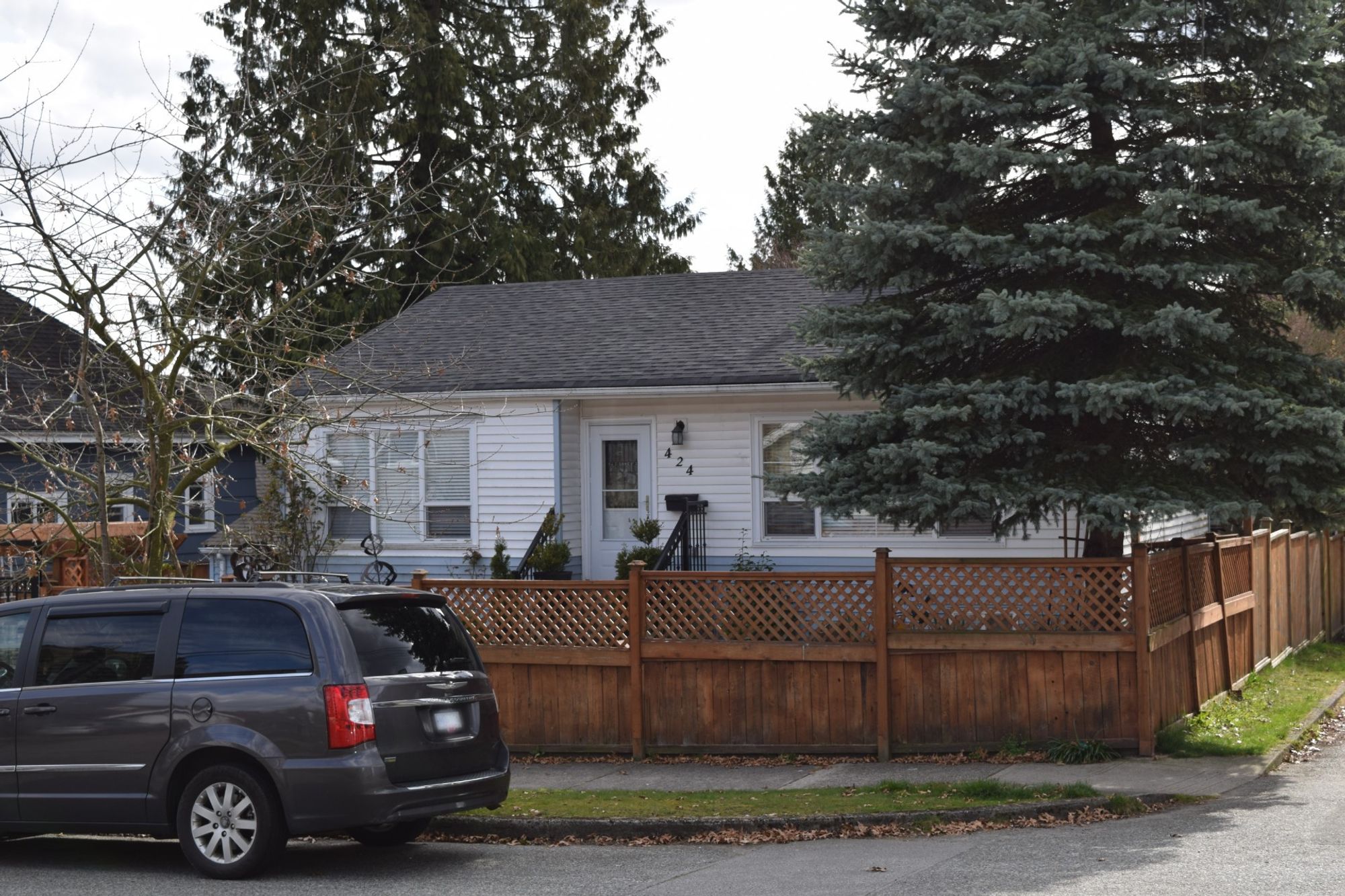 white single family house on corner lot with large tree in yard and surrounded by a wooden fence