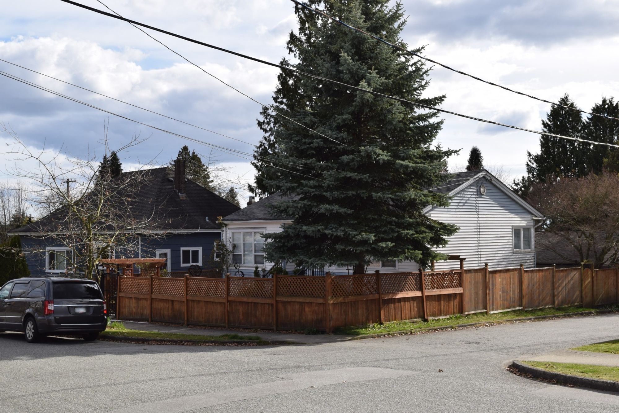 white single family house on corner lot with large tree in yard and surrounded by a wooden fence