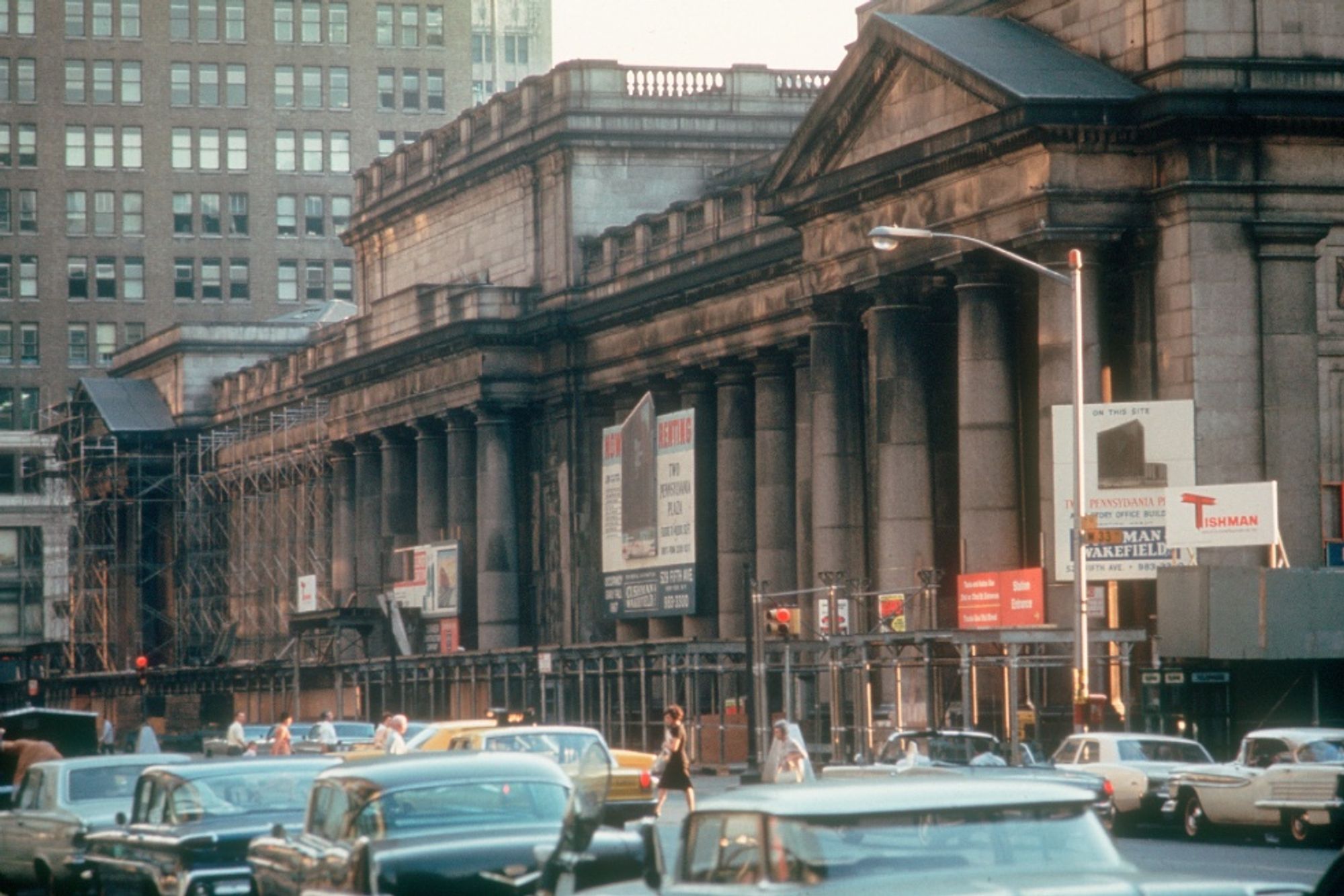 Old Penn Station surrounded by scaffolding, Tishman Wakefield signs, & dual aspect traffic lights.