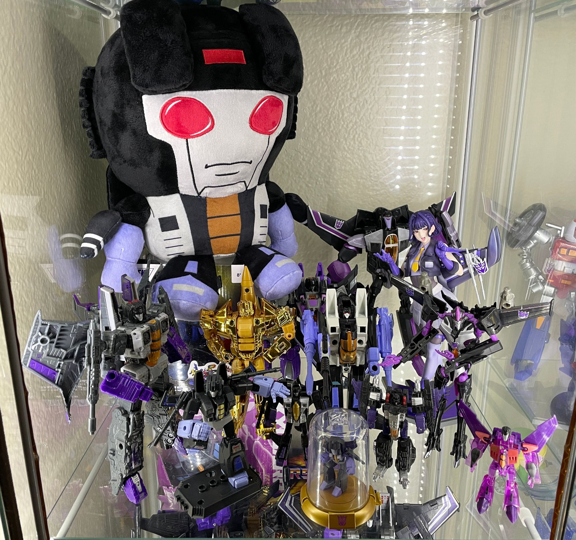 A display shelf full of Transformers Skywarp figures. Few more G1-styled designs, the Animated version, the Bishoujo statue, the import Prime figure, the recent Blokees figure, and a few others. There's a big ol' plush Skywarp in there, too.