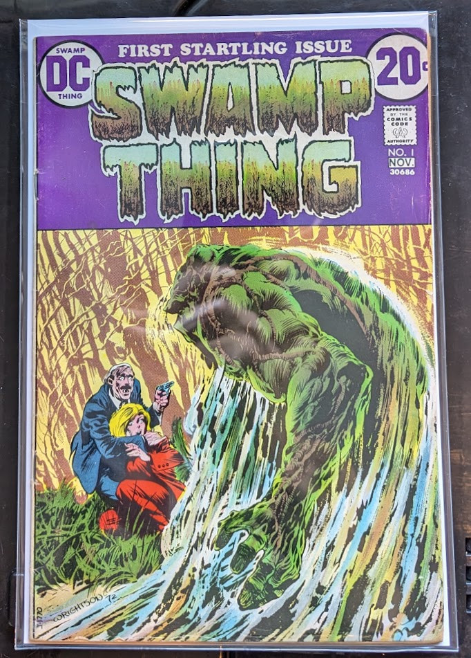 Art by Berni Wrightson

Swamp Thing pulls himself out of the water at the edge of a swamp, towards a blonde haired woman who is being held by a bald man in a suit who has a gun 