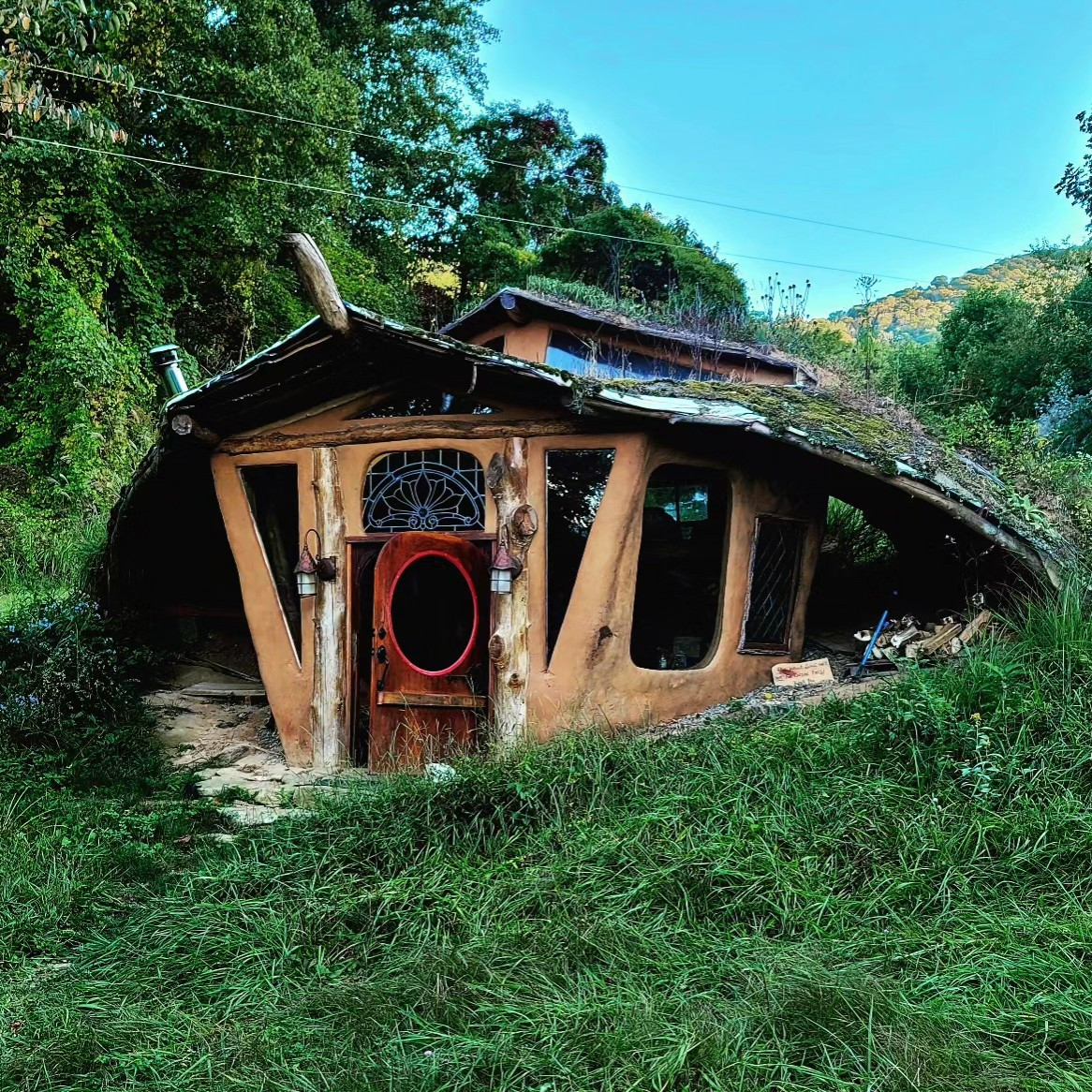 Hobbit House in green pasture with mountains in background