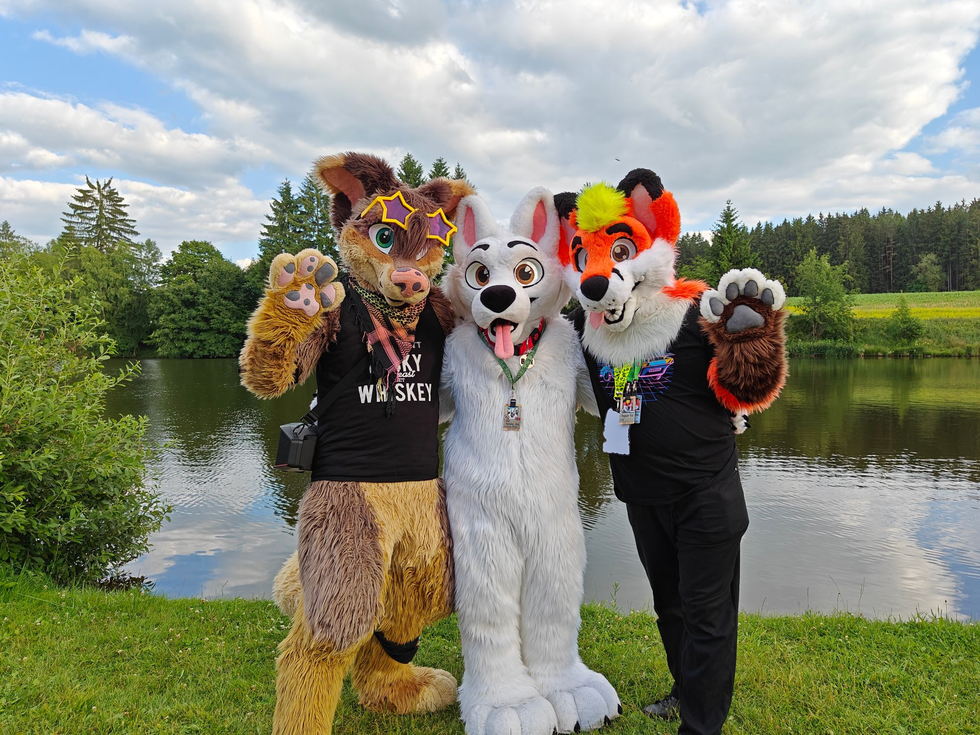 An anthropomorphic coyote, a dog and a fox near a pond in Czechia at Cesfur 2023 happily waving to the camera