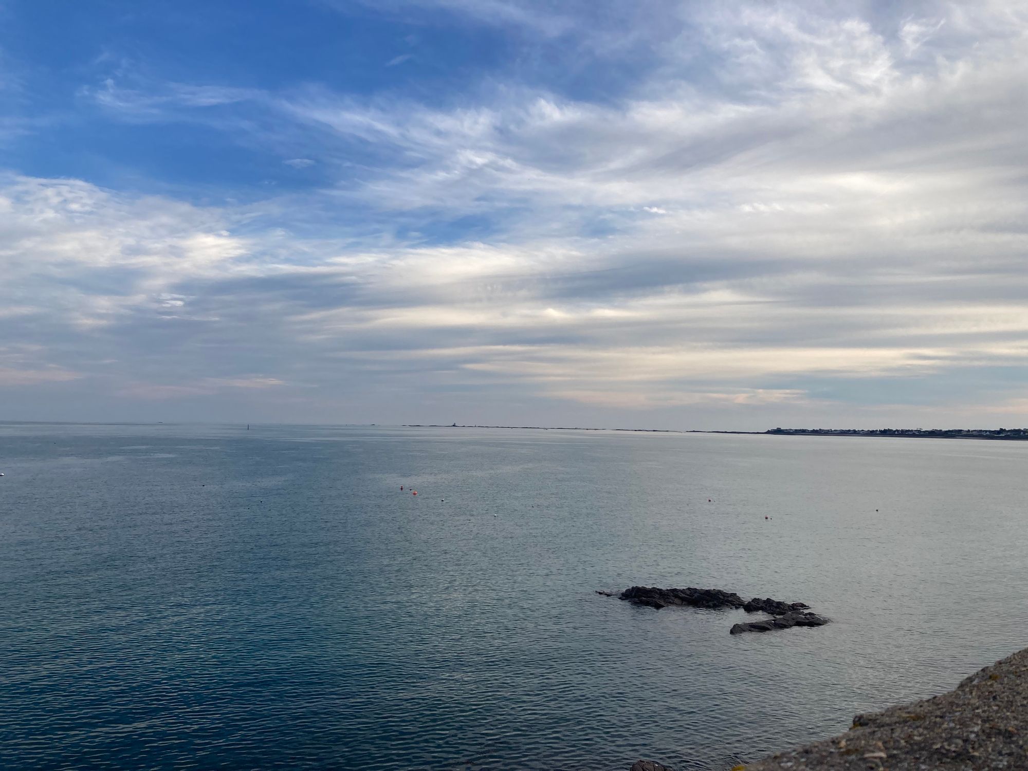 The sea can be seen on the lower half of the photo, on the left are some rocks, and above are beautiful blue skies with clouds.