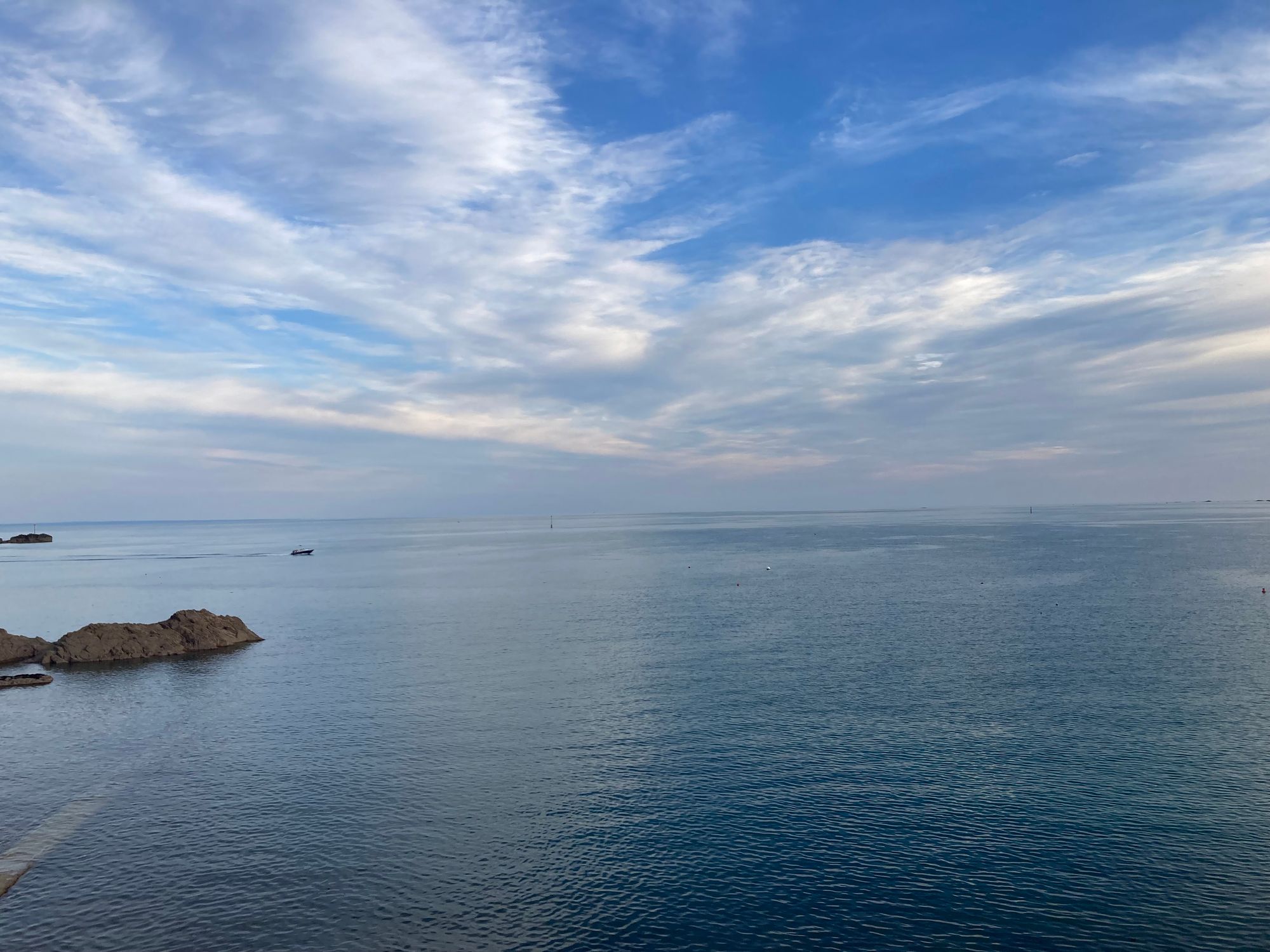 The sea can be seen on the lower half of the photo, on the left are some rocks, and above are beautiful blue skies with clouds.