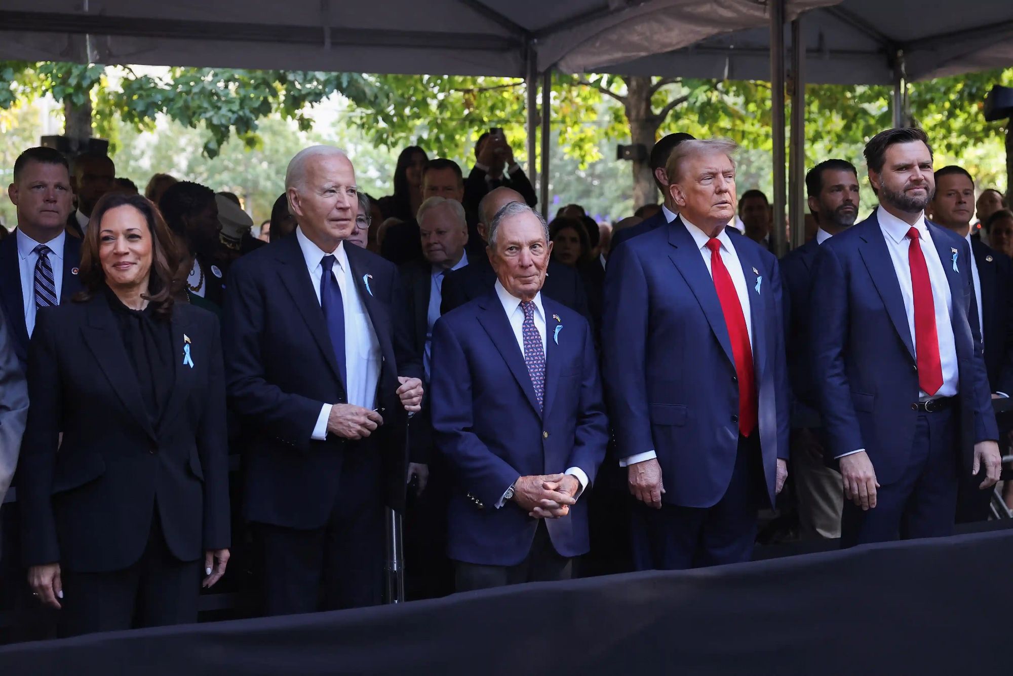 Kamala Harris and Joe Biden are at the 9/11 memorial ceremony wearing dark clothes. Donald Trump is in a blue suit with a bright red tie with a tiny knot, standing next to him is JD Vance wearing AN IDENTICAL SUIT AND RED TIE WITH A TINY KNOT