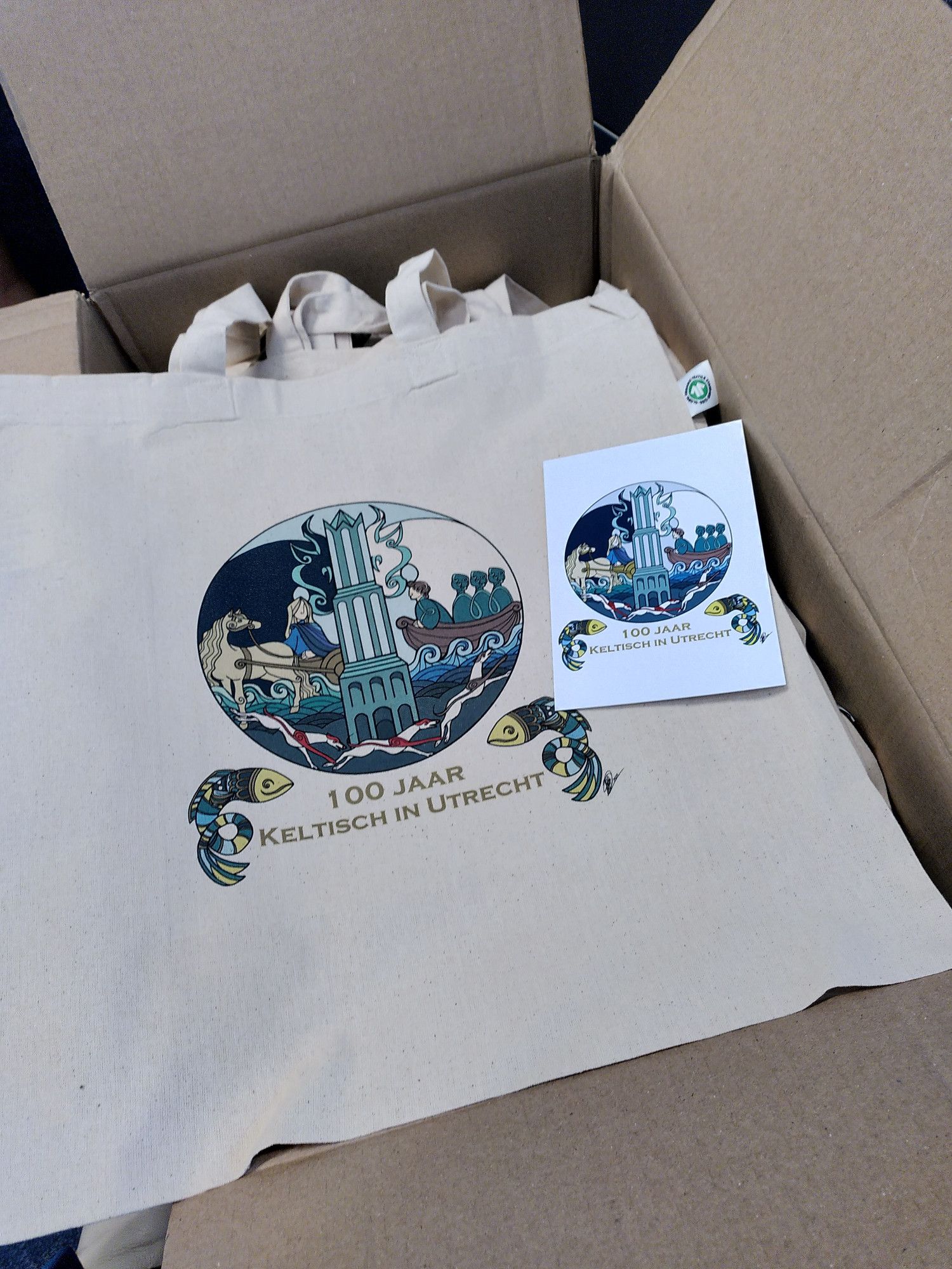 Logo of the Centenary of Celtic Studies in Utrecht on a bag and a post card: it shows the Dom tower as well as four monks in a boat, red-white dogs, and a woman in a chariot.